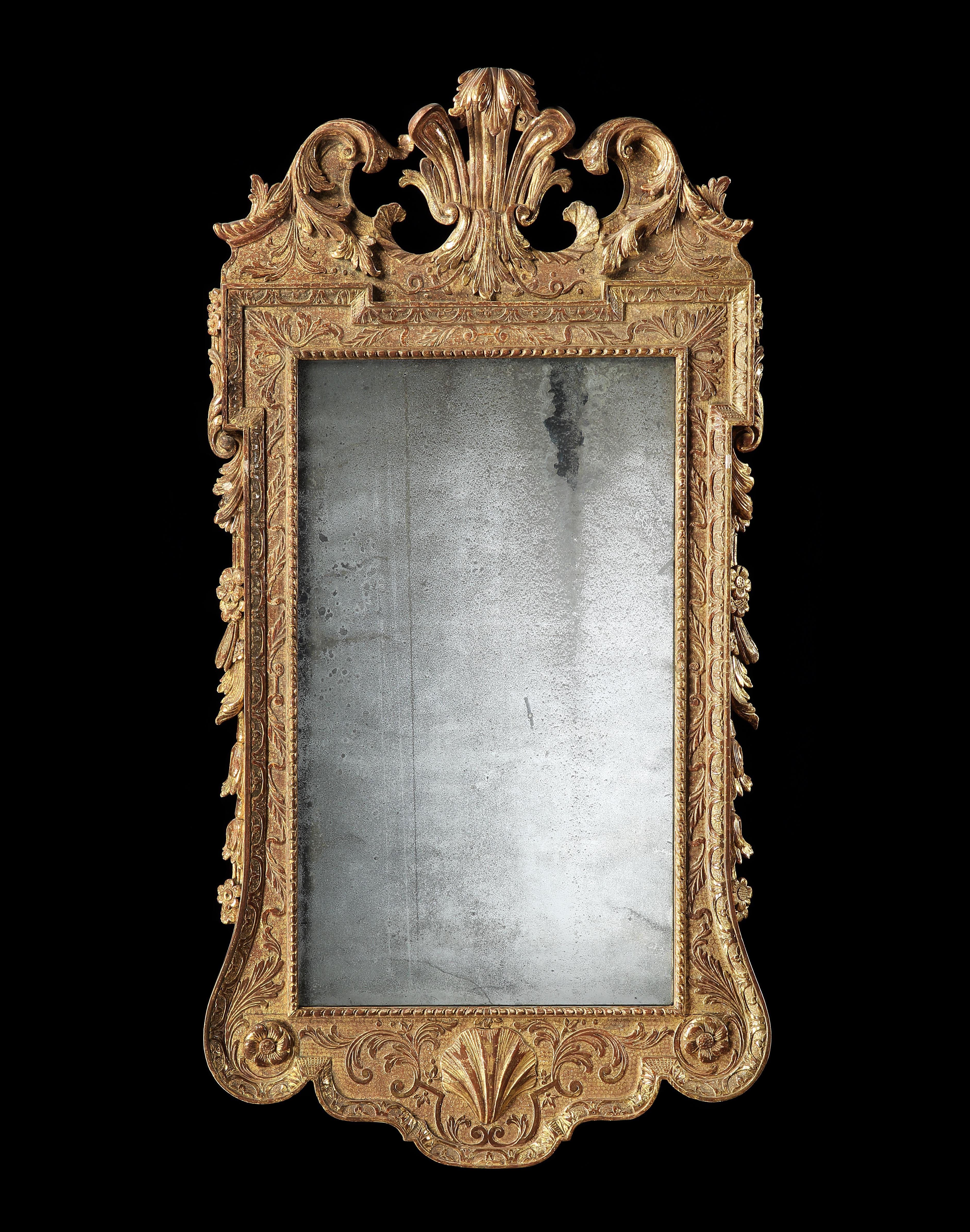 A George II carved and gilded mirror the shaped top centred by a shell, above the original mirror plate inset by a boarder carved with acanthus leaves and egg and dart carvings, the mirror framed with side swags to both sides depicting rosettes. The