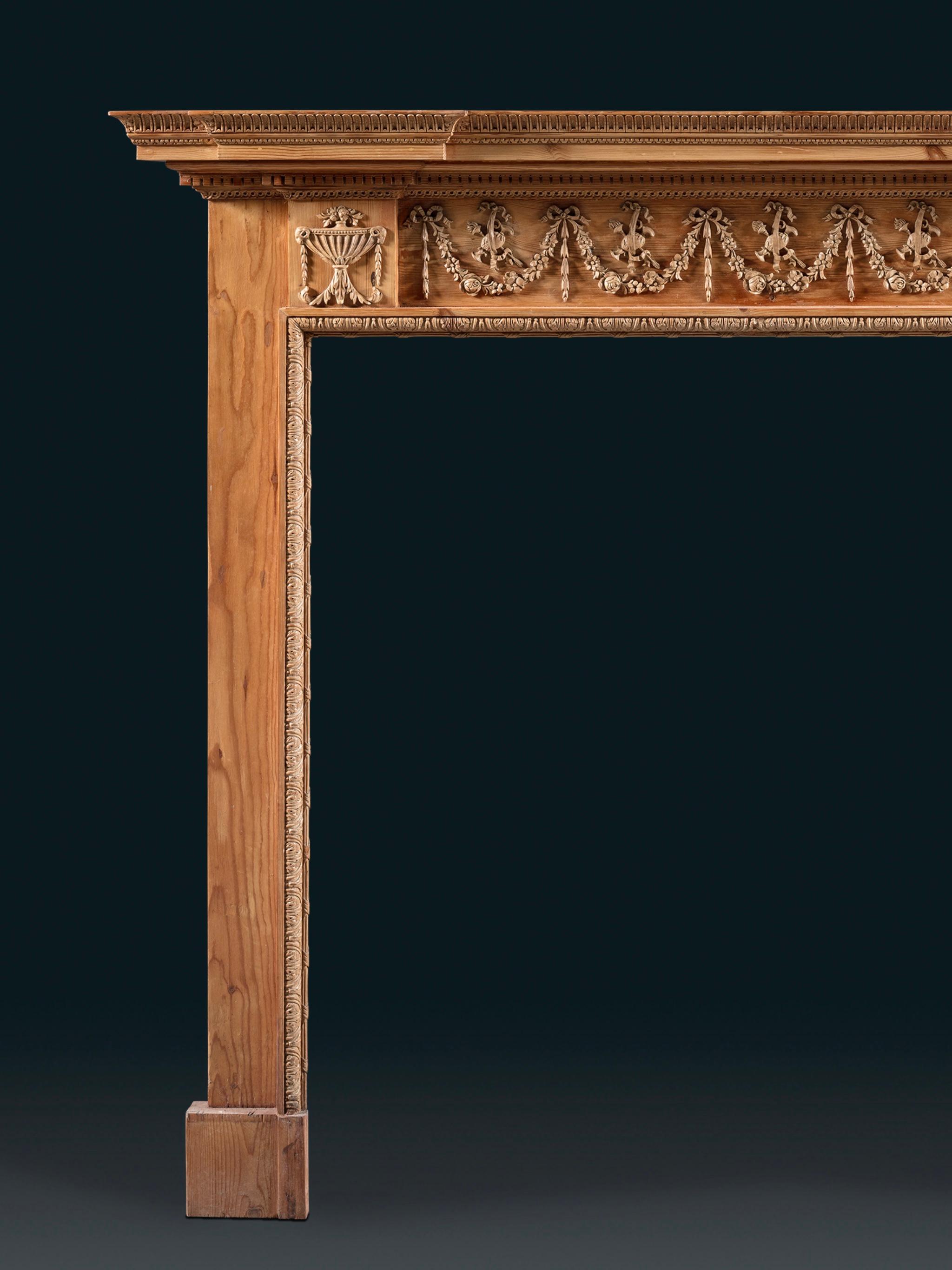 Cheminée en pin et gesso de la fin du XVIIIe siècle, finement dessinée, avec une étagère à l'avant et une frise représentant un motif de cruches croisées et de torches enflammées. Sur les blocs d'angle sont sculptées des urnes de style Adams avec