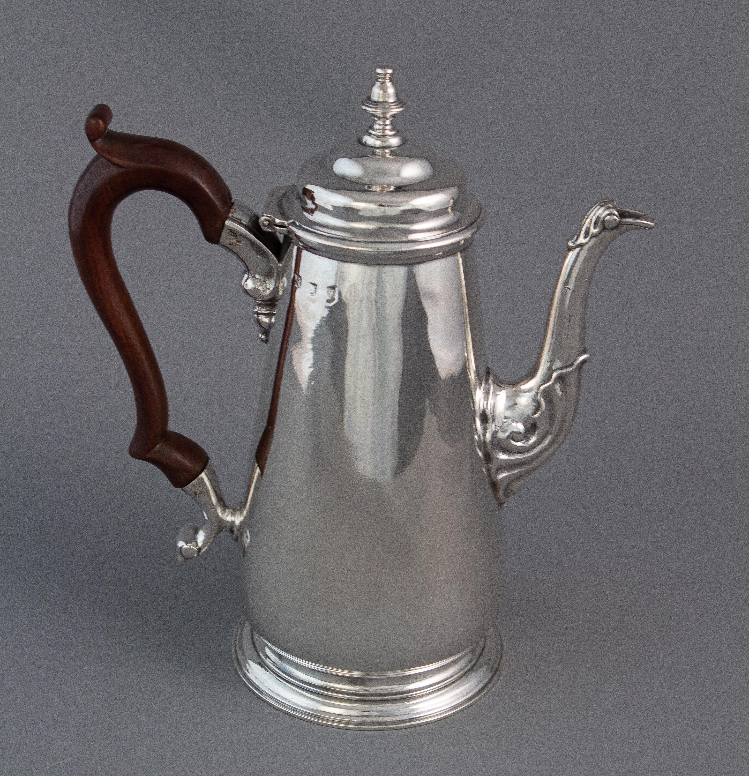 A George II silver coffee pot, London 1735 by Augustin Courtauld. The baluster form body with a scroll decorated cast spout and handle mountings. The stepped and domed lid surmounted with a cast acorn finial. With a scrolling fruitwood handle. All