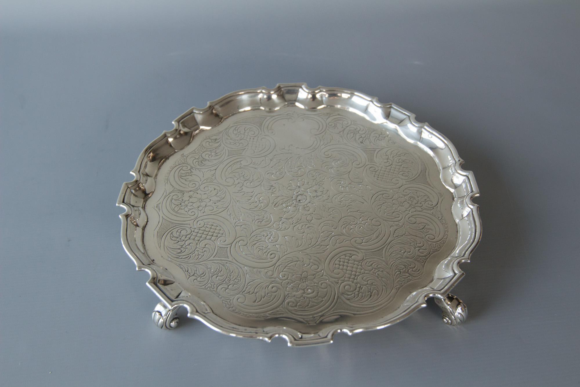 A very fine silver salver of circular form with shaped rim and the whole resting on four scroll feet. The center embossed & chased with foliate scroll decoration. 

Hallmarked for London 1734 by George Hindmarsh. 

This is in superb condition