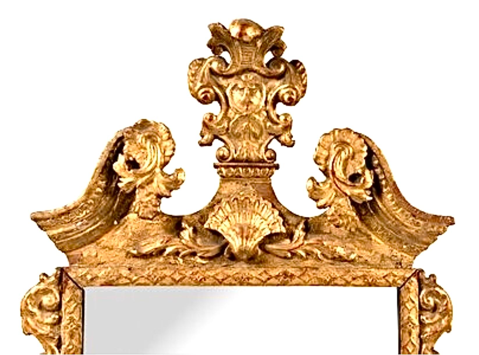 George II Giltwood Mirror. Mirror features beveled edges and is mounted in a gilt frame. Carved with scrolling acanthus leaves. Mirror has a geometric-carved border, surmounted by an acanthus-carved broken arch pediment centered by a foliate