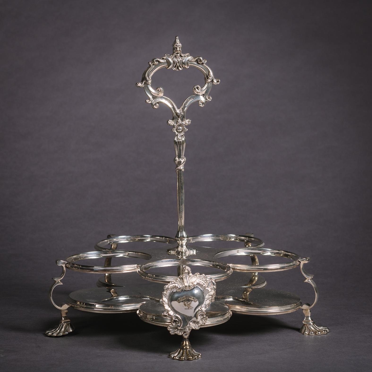 Una raffinata ampolla Warwick placcata in argento in stile Giorgio II.

Il vassoio a cinque foglie ha un'alta maniglia centrale con una presa a foglia e figurativa sopra una cornice con un cartiglio armoriale rococò.  È sollevato su quattro gambe a