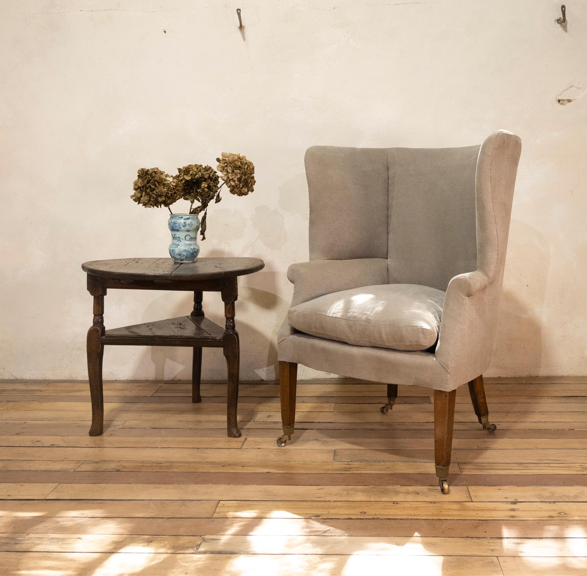 A George III barrel back chair. Upholstered in a lovely grey linen with interior tub-back wings and elegant hand stitches decoration to the seams. Displaying out-scrolled arms and a loose feather seat cushion covered in Pale Gray linen. Raised on