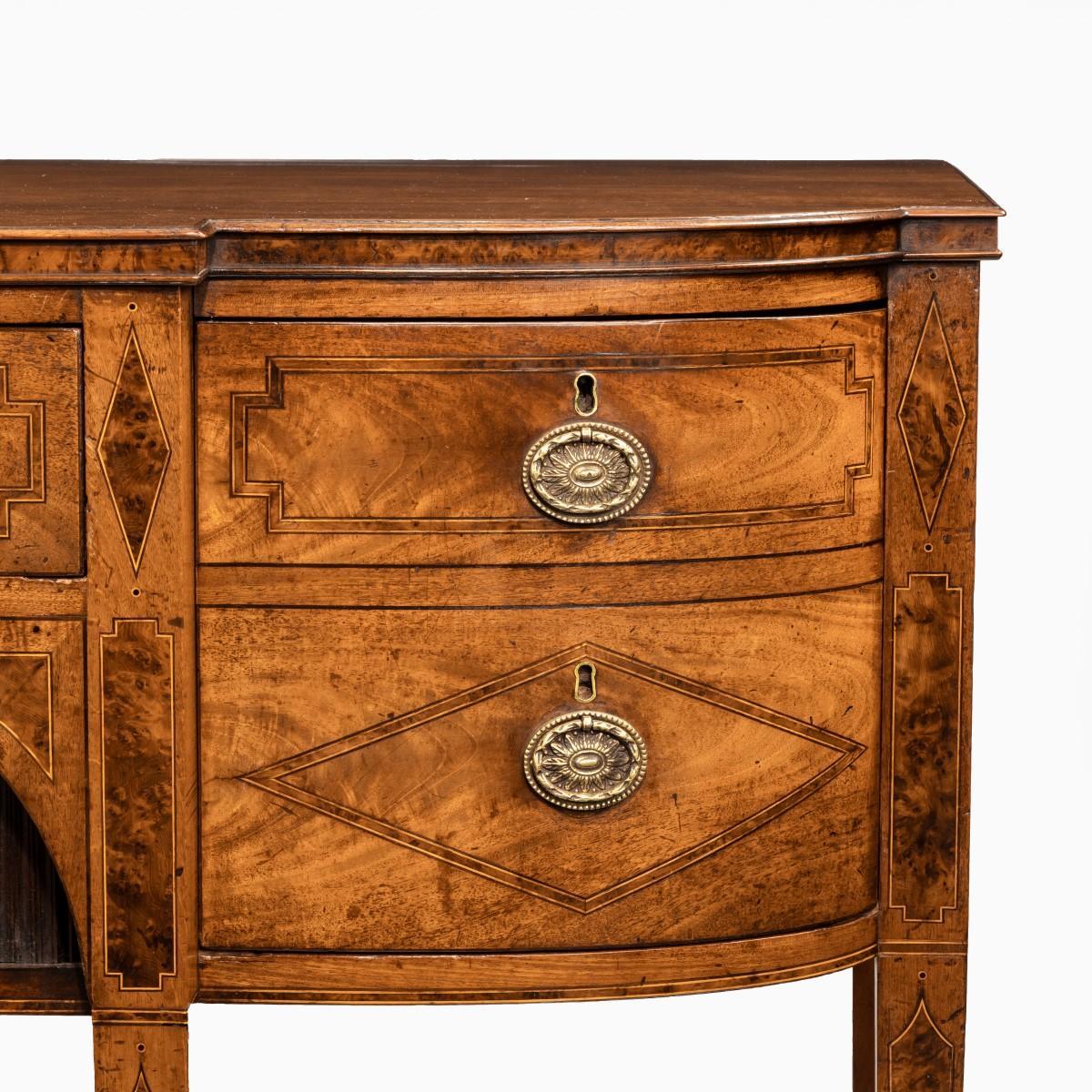 A George III breakfront yew-wood inlaid mahogany sideboard, of rectangular form with a central frieze drawer above tambour cupboard doors between further cupboards with dummy drawers and a single deep drawer, the left side return with a small