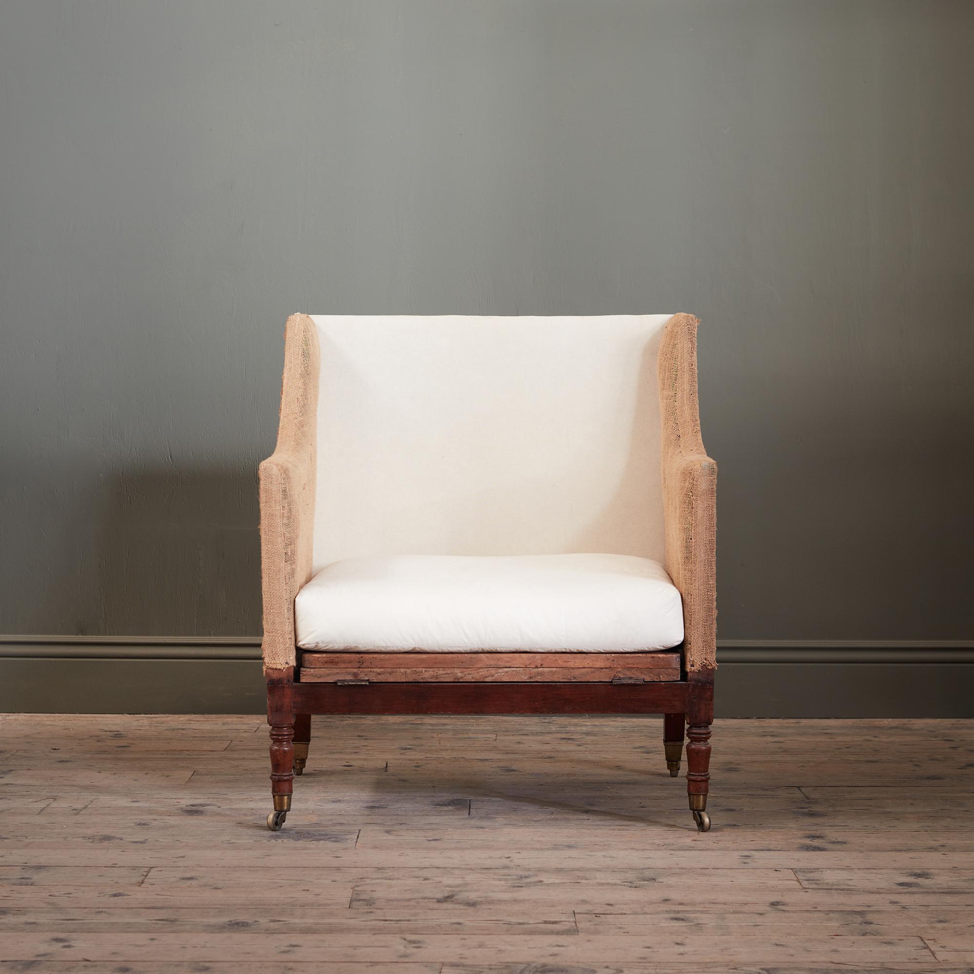 The wide upholstered frame raised on turned mahogany legs with brass castor, folding hinged & extending pine bed frame with screw in turned mahogany legs, three down filled cushions. Butler advertised this chair as : ‘Upon the best and most approved