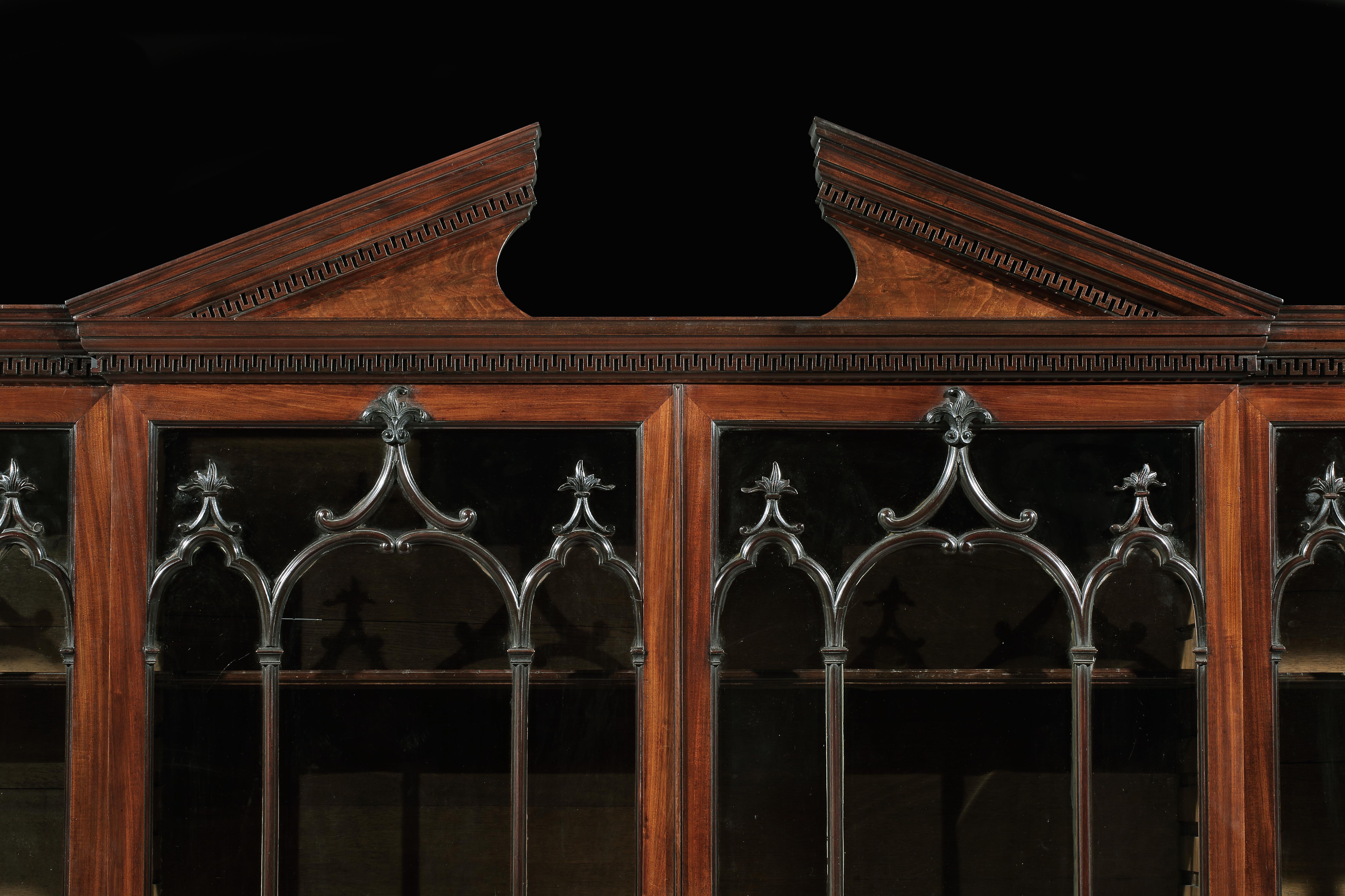 A superb George III Chippendale period mahogany breakfront library bookcase, the raised architectural pediment, with a detailed moulded edge, above arched Gothic glazed doors carved with acanthus, resting on a raised paneled door base with a deep