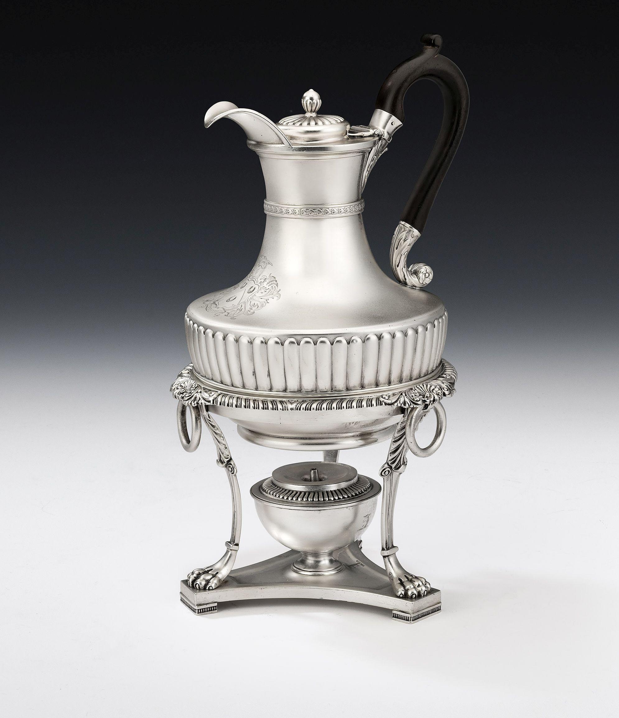 This important jug is modelled in the Regency Classical revival style. The main body has a pyriform body decorated with an unusual wide lobed band, which acts as a projecting ledge to support the jug on its Stand. A band of fruiting berries