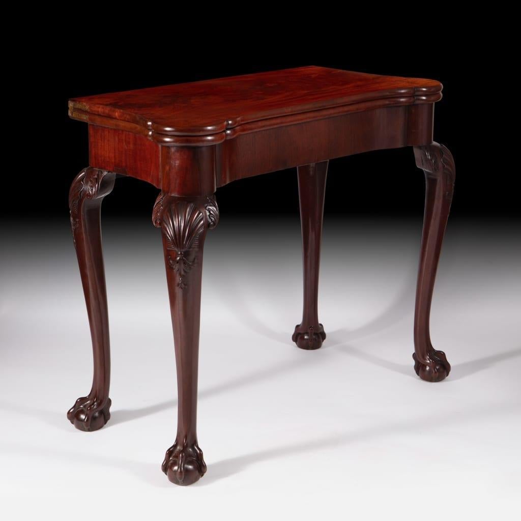 A fine mid-18th-century rich mahogany George III card table raised on cabriole legs with ball and claw feet, scallop shells carved in high relief on all four legs with swags, supporting a folding top opening to baize with sunken counter