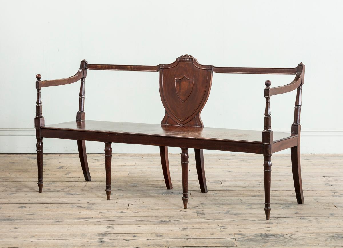 Banc d'entrée en acajou de George III, avec un dossier élancé et mouluré, des accoudoirs tournés et une assise solide rectangulaire, avec quatre pieds avant tournés et effilés.

Un exemple similaire du début du XIXe siècle se trouve à Trinity House,