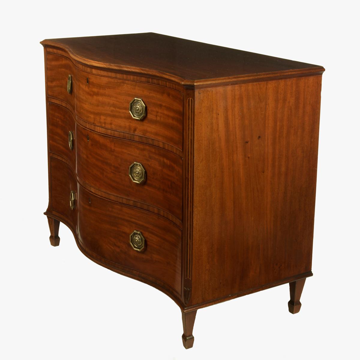 A George III mahogany serpentine chest of drawers, with three long graduated drawers flanked by canted and line-inlaid corners with octagonal brass handles, raised on conforming square tapering legs and spade feet. English, circa