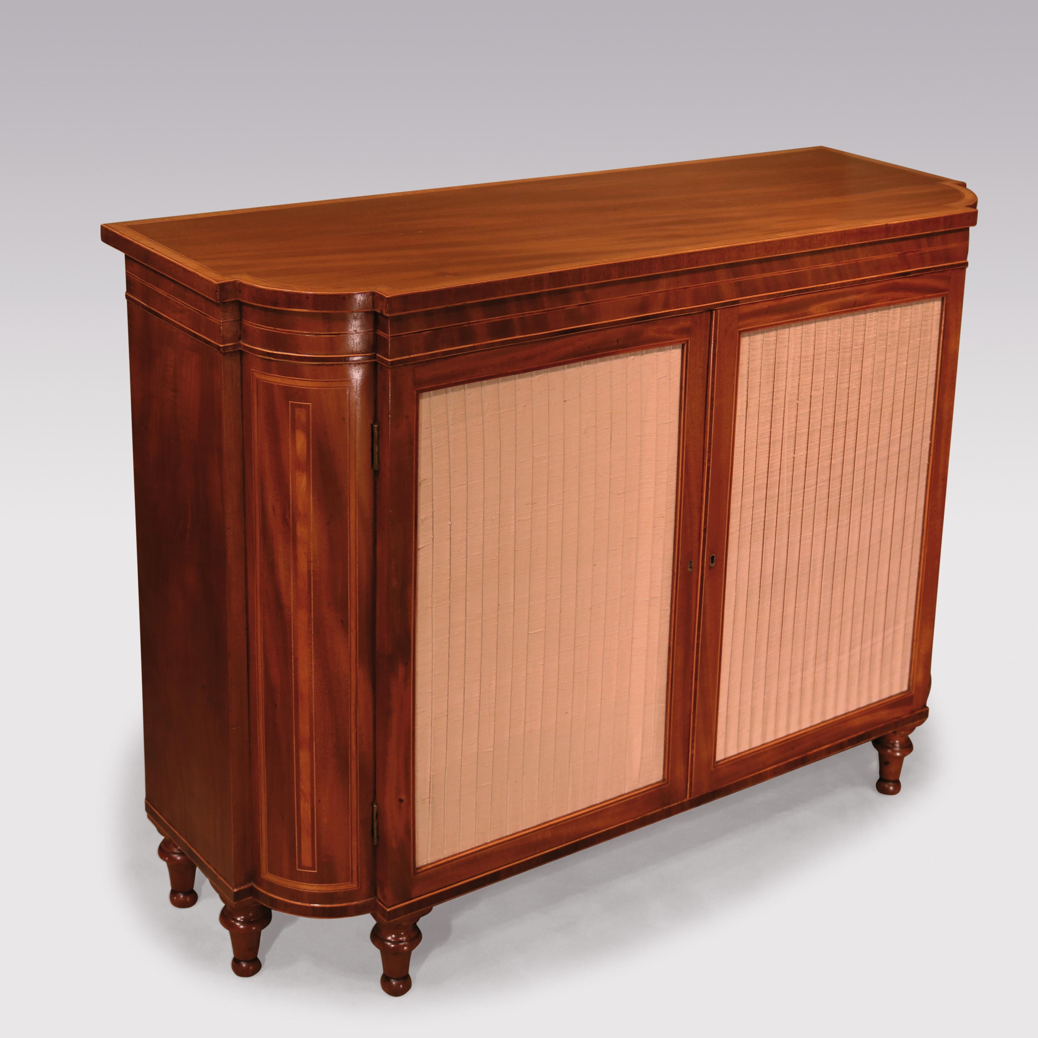 A George III period well figured and faded mahogany two-door cabinet, with box-wood and ebony lined stringing throughout, having a satinwood cross-banded breakfront top, above two pleated silk-lined doors flanked by inlaid ‘rounded ’sides, supported