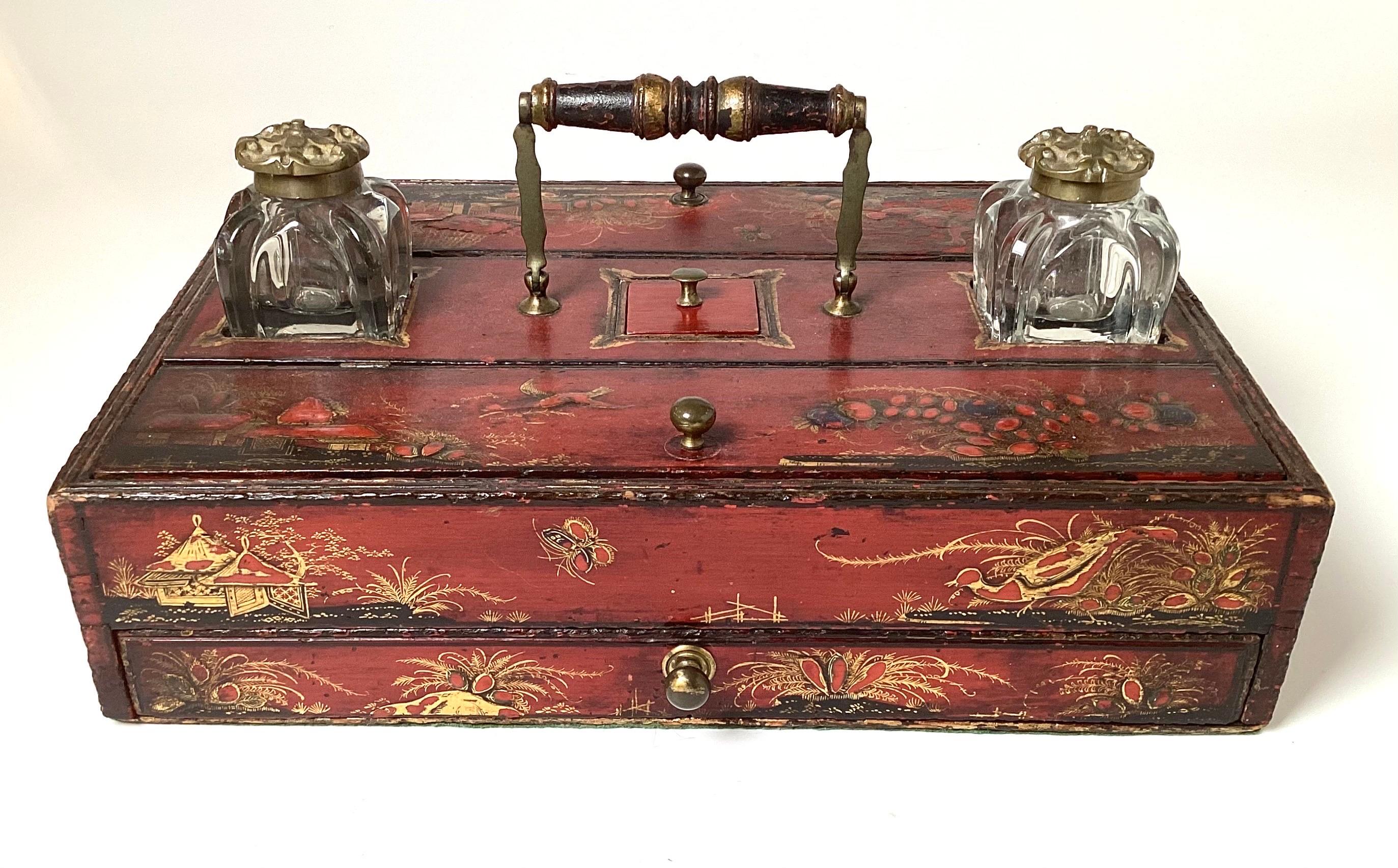 A hand painted red japaned ink stand with two French molded glass inkwells.  The top with lifting compartments for pens, and stamps, the bottom with a pull out drawer for paper.  Original condition showing expected age and use. 