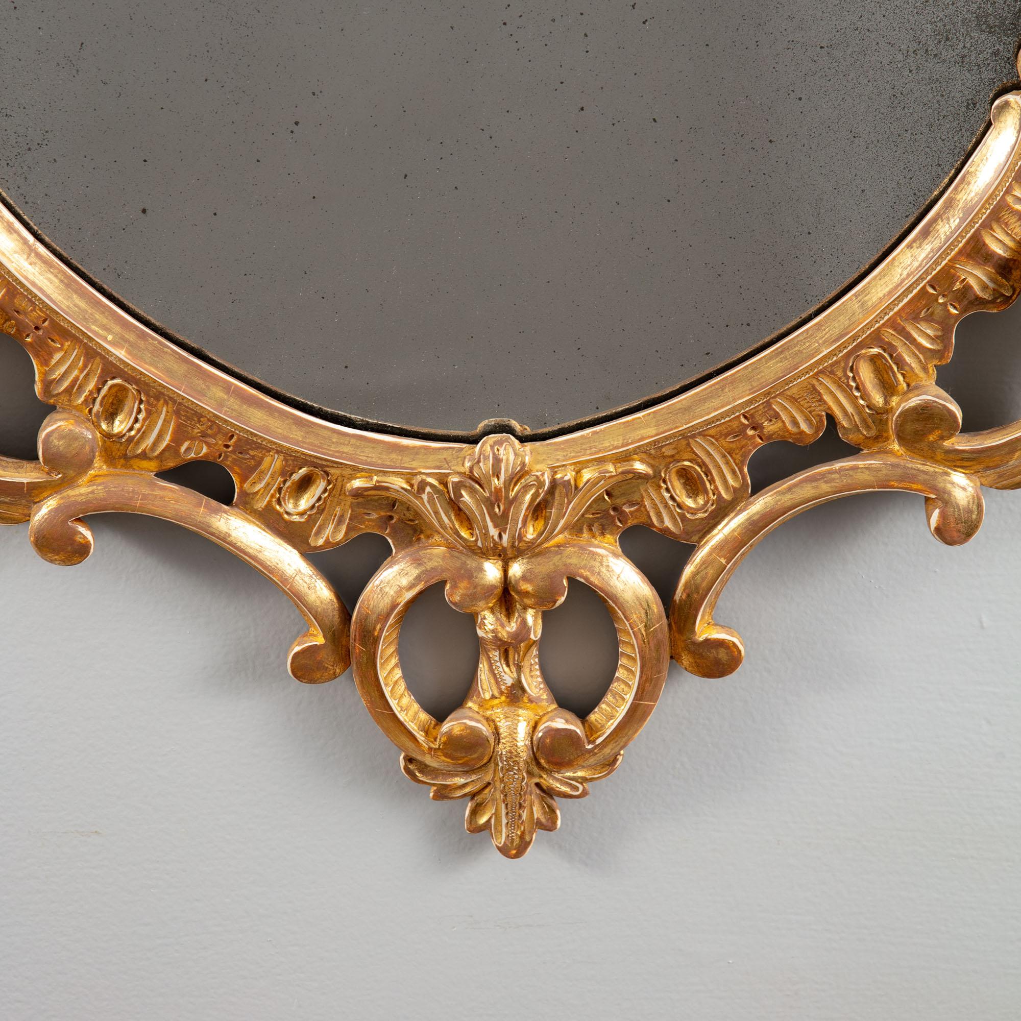 An elegant oval giltwood mirror from the second half of the 18th century. The oval outline composed with C and S scrolls, rocailles and swags of foliage and flowers, the apex with branches as the Prince of Wales feathers.

England, circa