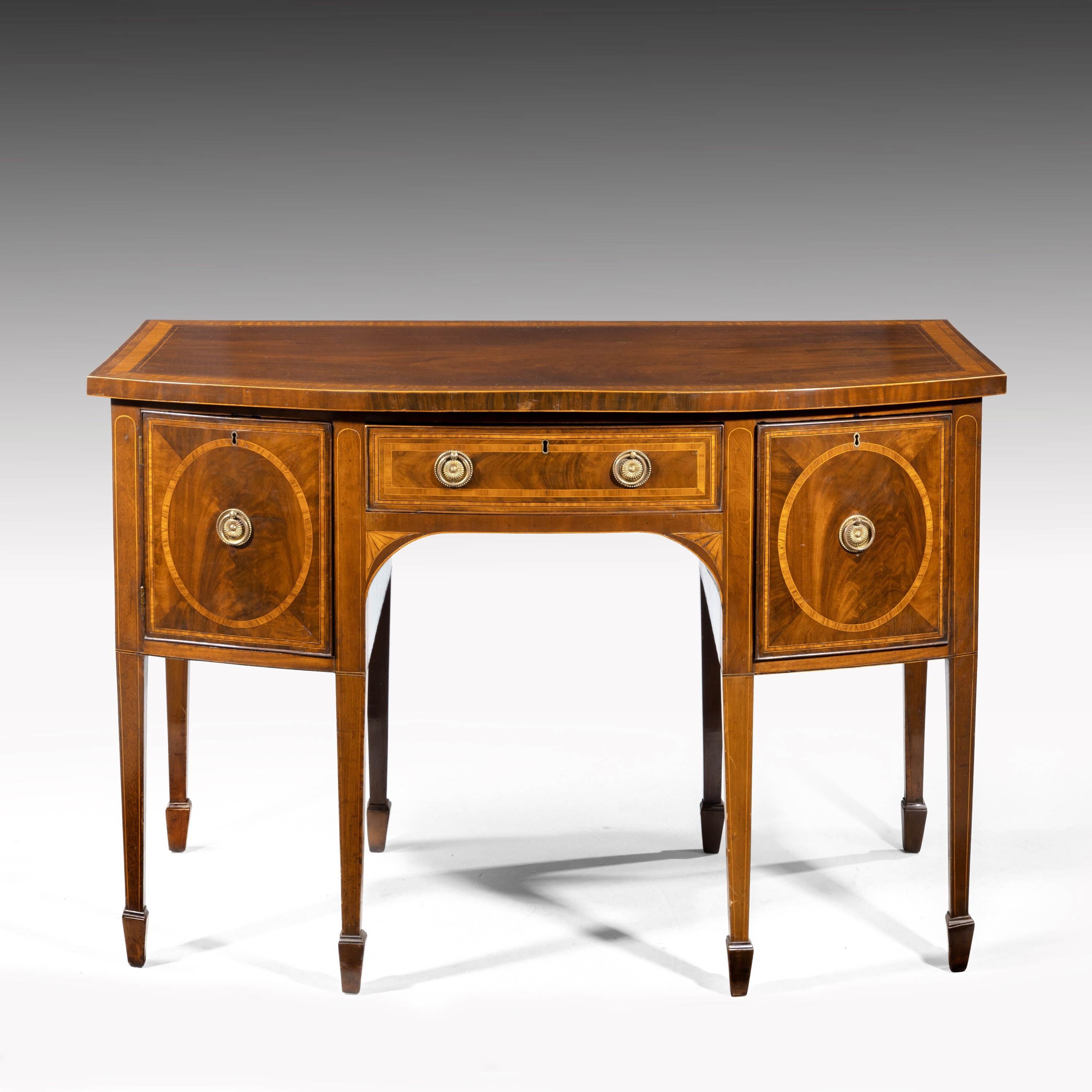 A George III Sheraton period mahogany bow front sideboard. With fine crossbanding work in boxwood string. With other timbers. Quartered drawer fronts to the left and right hand side. On fine, chamfered, tapering supports ending in block feet.
 