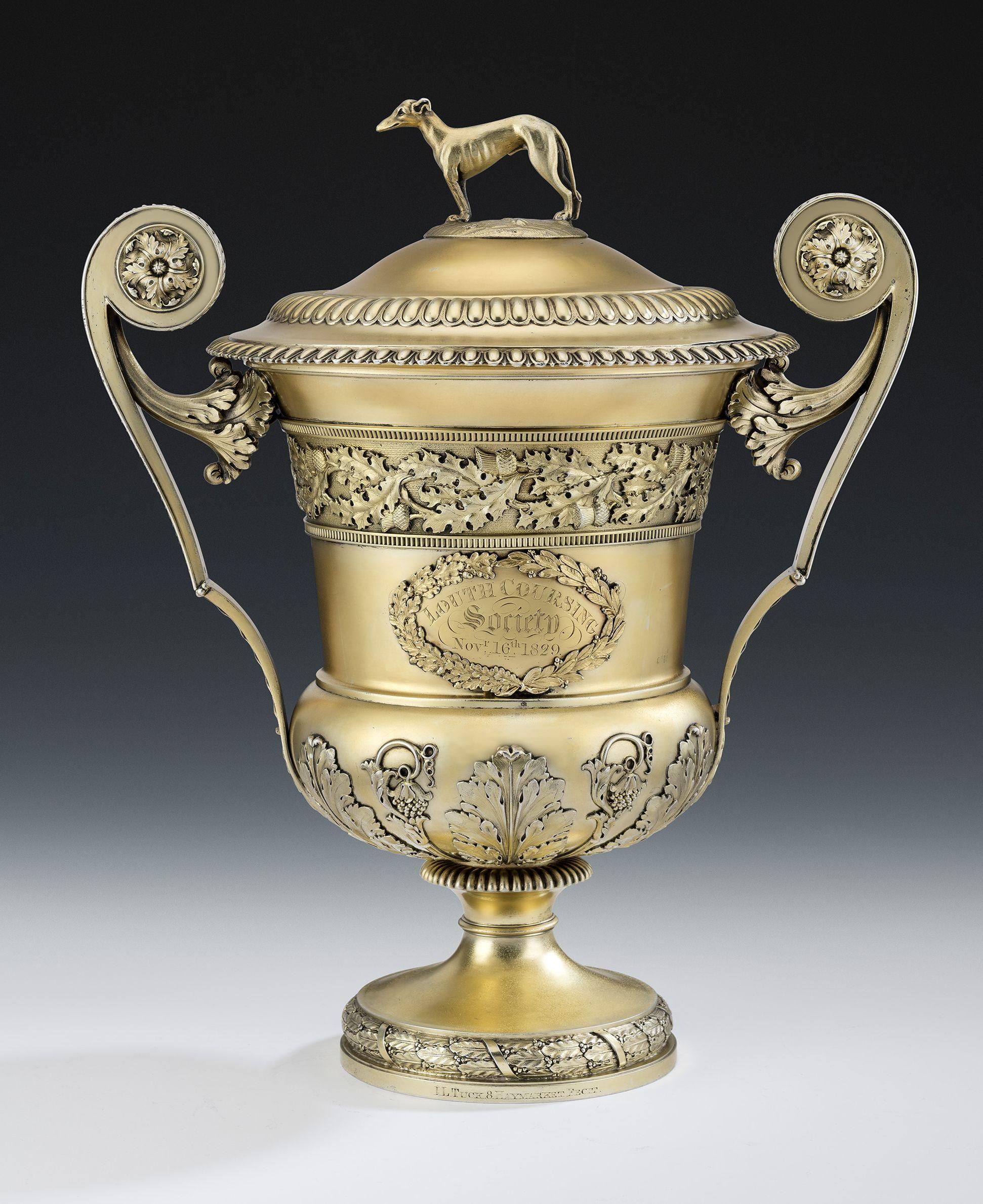 This important, and very unusual, George III silver gilt cup and cover, or wine cooler, was made in London in 1815 by William Elliott. This exceptional piece stands on a circular pedestal foot which is decorated with a tied laurel leaf and berry
