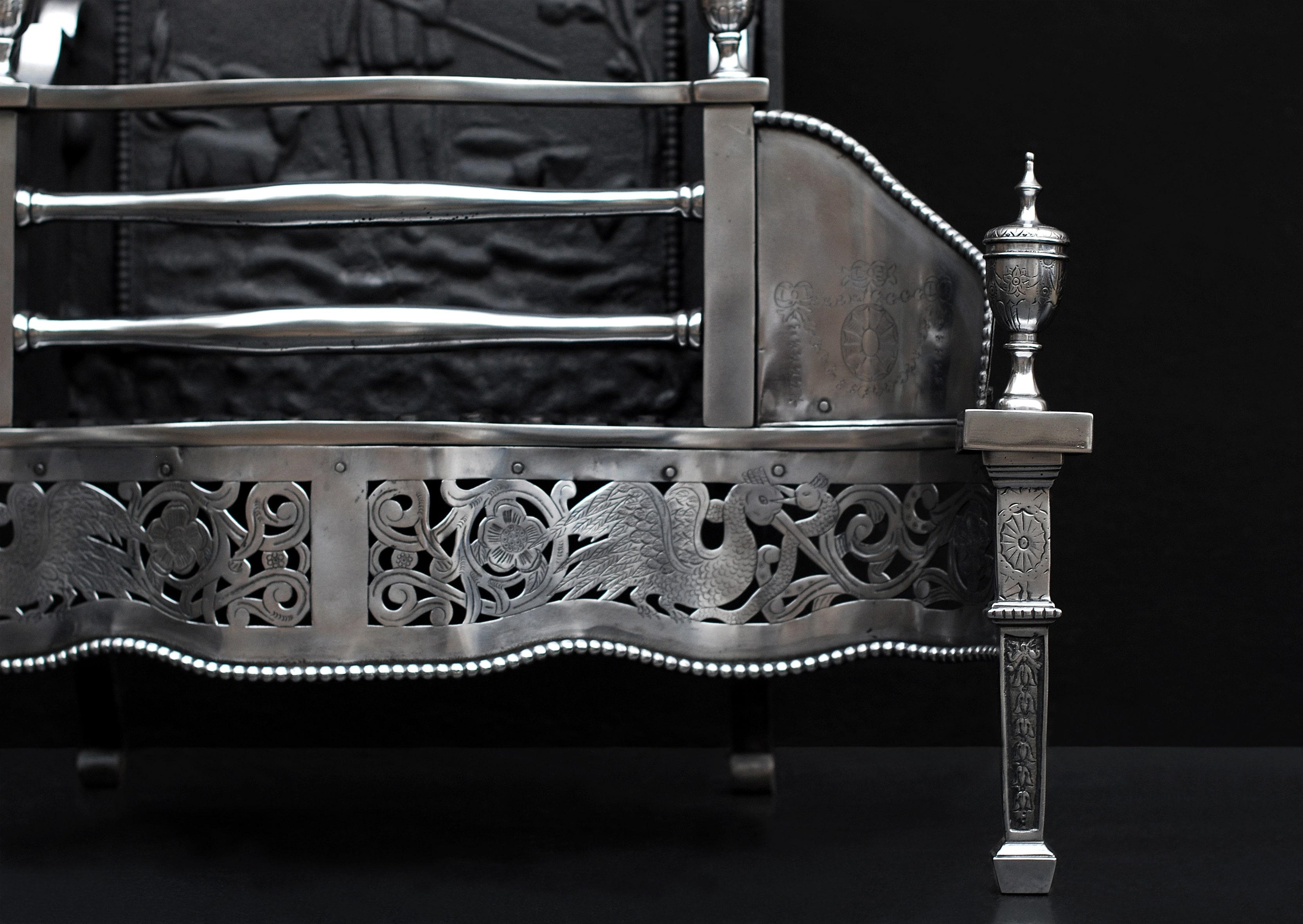 A George III style polished steel firegrate. The deep fret nicely pierced and engaved with storks and flower, the wings engraved with swags and ribbons. Engraved urn finials and tapering legs with patera and bell flowers. Decorative shaped back with