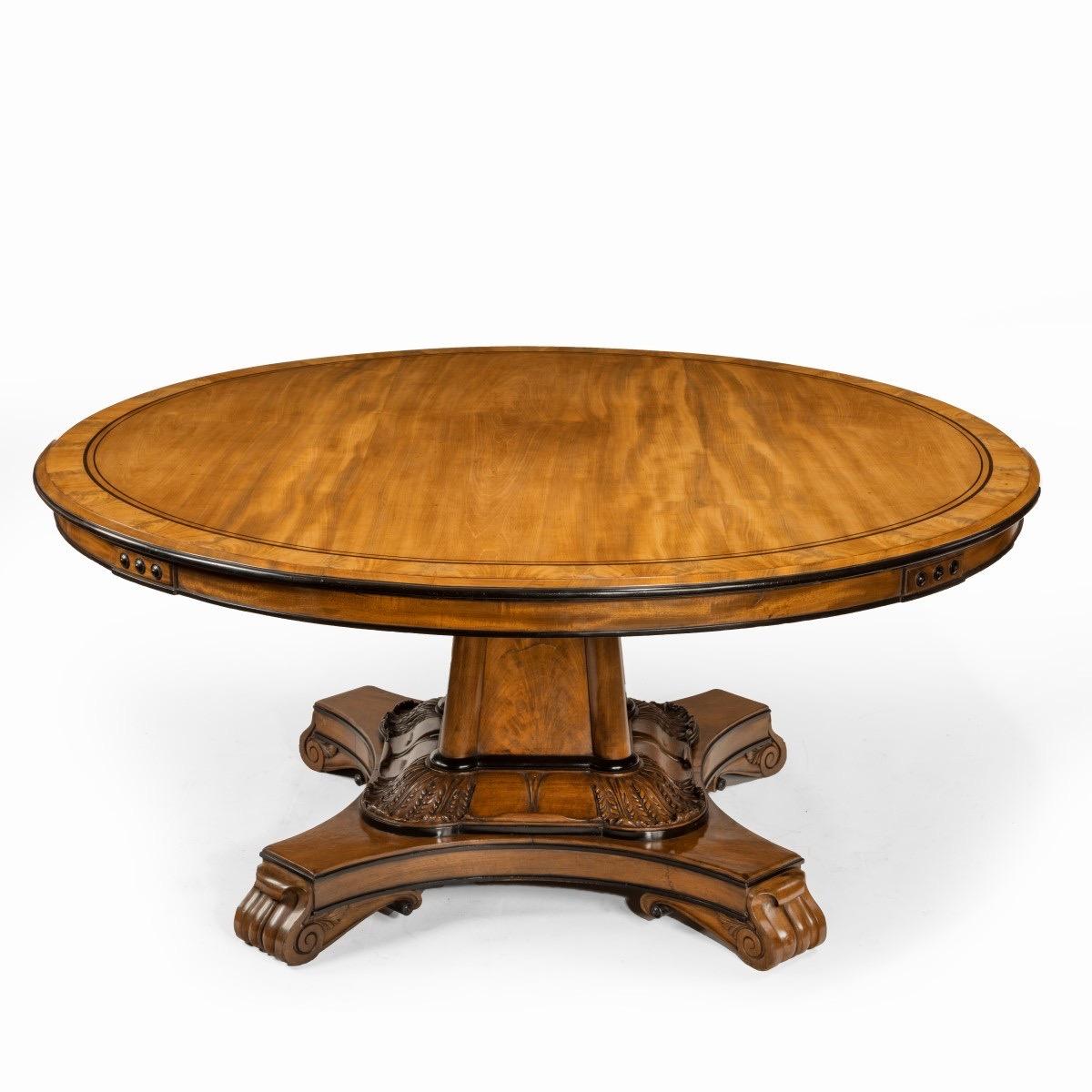 A George IV ebony-inlaid mahogany tilt-top centre table, the circular top with a flame-veneered cross-banded border above a moulded frieze with ebony stringing and four small rectangular plaques inset with three ebony buttons, all raised on a