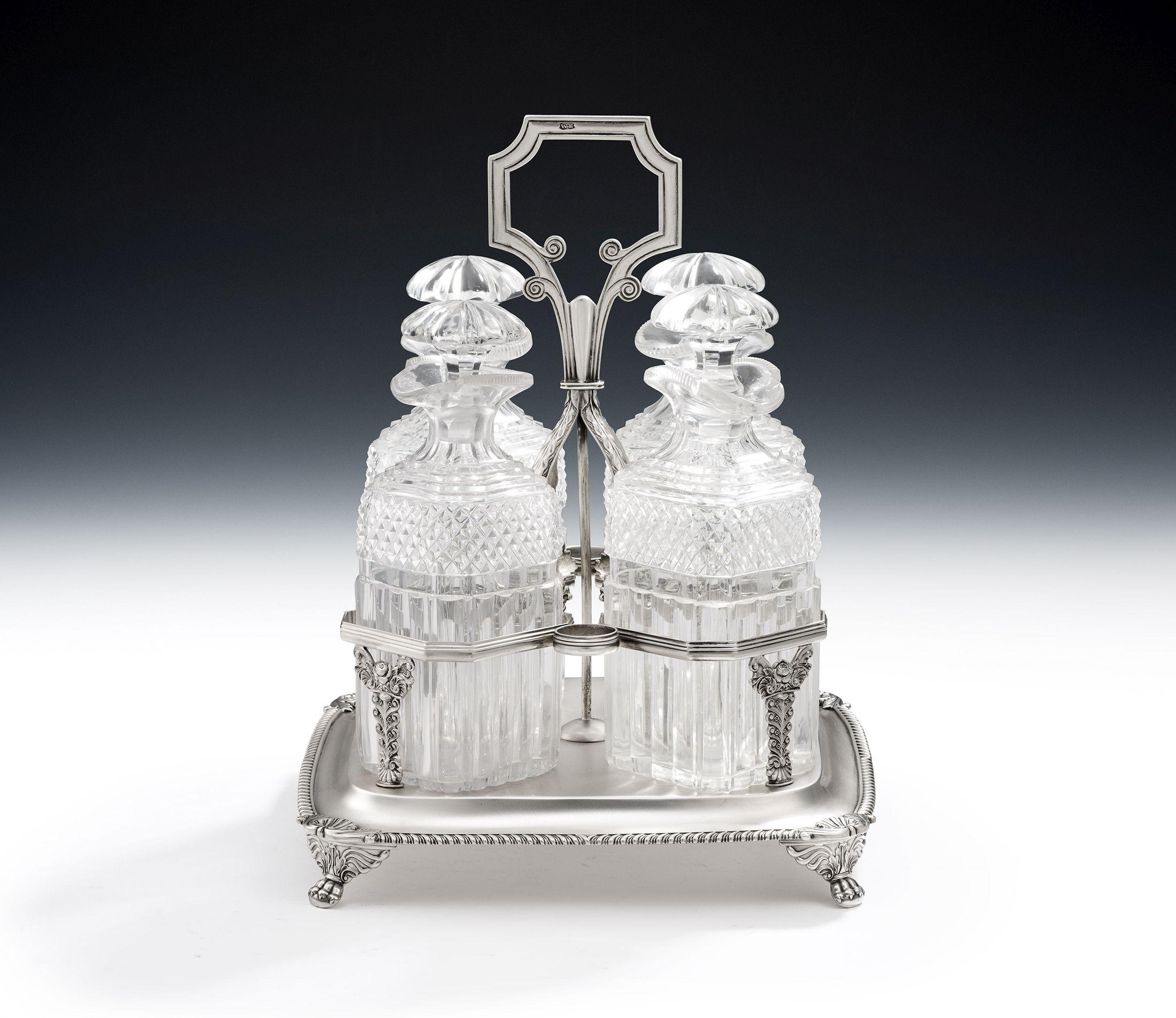 UN IMPORTANTE DECANTADOR DE CUATRO BOTELLAS DE GEORGE IV
HECHO EN LONDRES EN 1823 POR WILLIAM BATEMAN I

Esta rarísima pieza tiene una base de plataforma cuadrada con borde estriado, que muestra una concha rococó en cada esquina flanqueada por