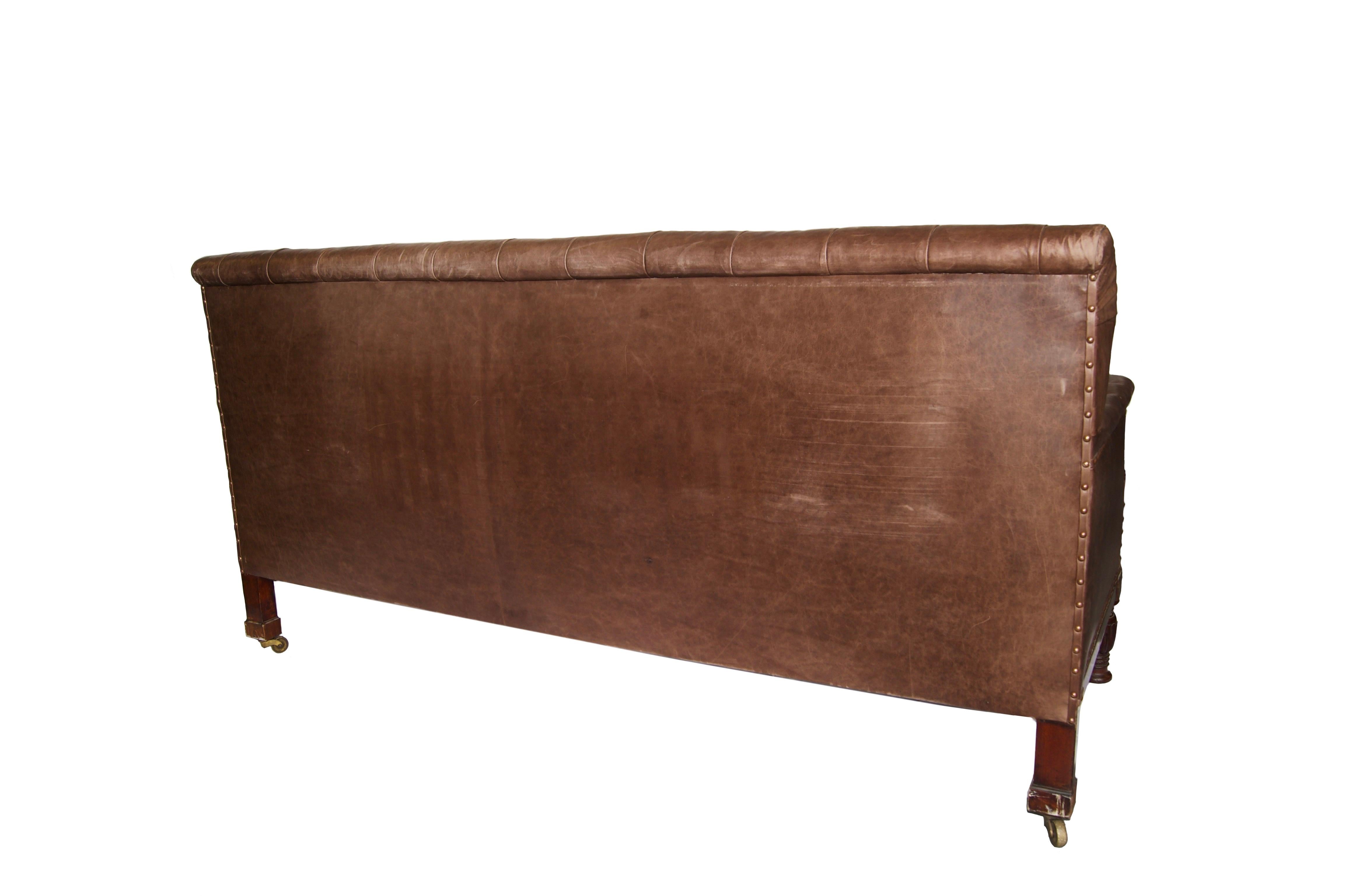 A George IV leather club sofa, early 19th century with straight back and arms, turned wood legs, upholstered in dark brown leather, button and stud detail.