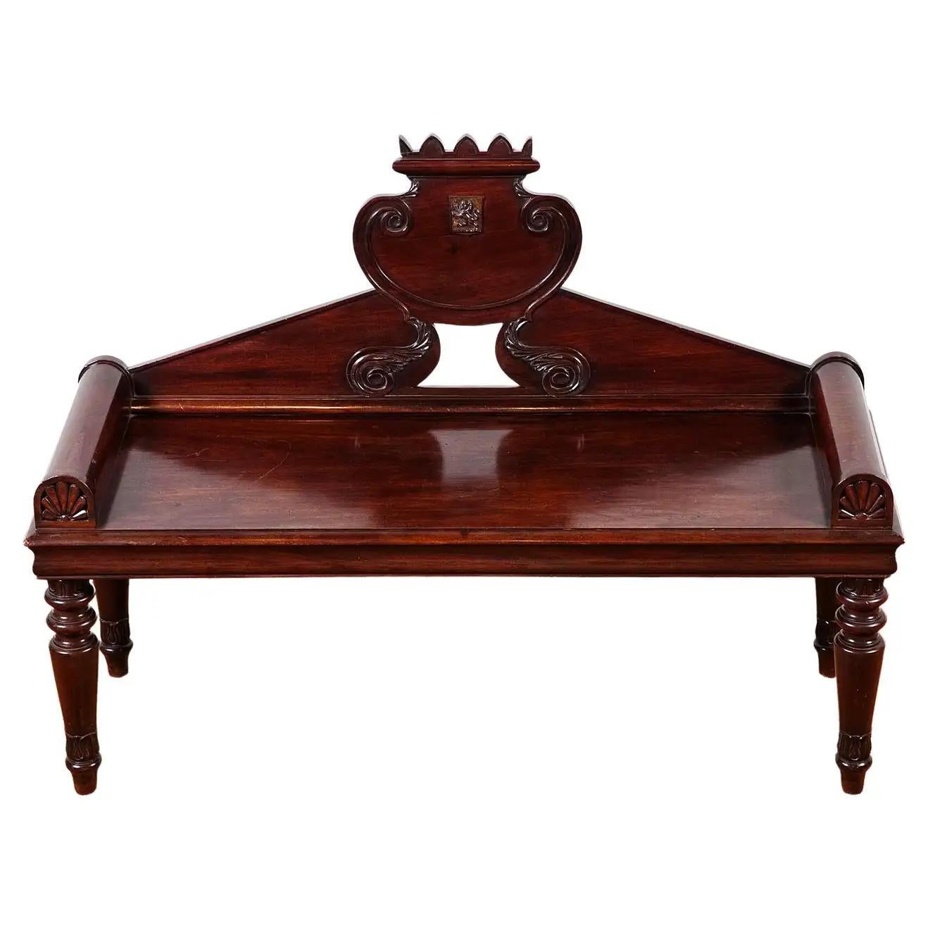 A George IV mahogany hall bench, the shield back with a castle top and central coat of arms, to a rectangular seat with roll arms carved with anthemions, resting on turned legs with lotus leaf carving.
Featured in the household furniture & interior