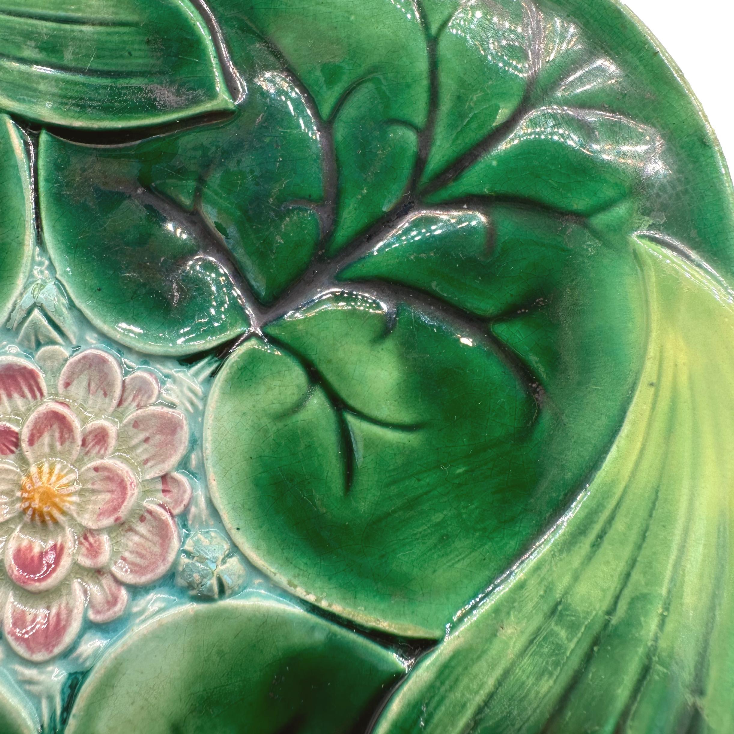 Assiette à lotus en majolique de George Jones, moulée de façon naturaliste comme des nénuphars et des feuilles de lotus se chevauchant, avec une fleur de lotus centrale rose et jaune moulée en relief sur de l'eau émaillée turquoise, le revers