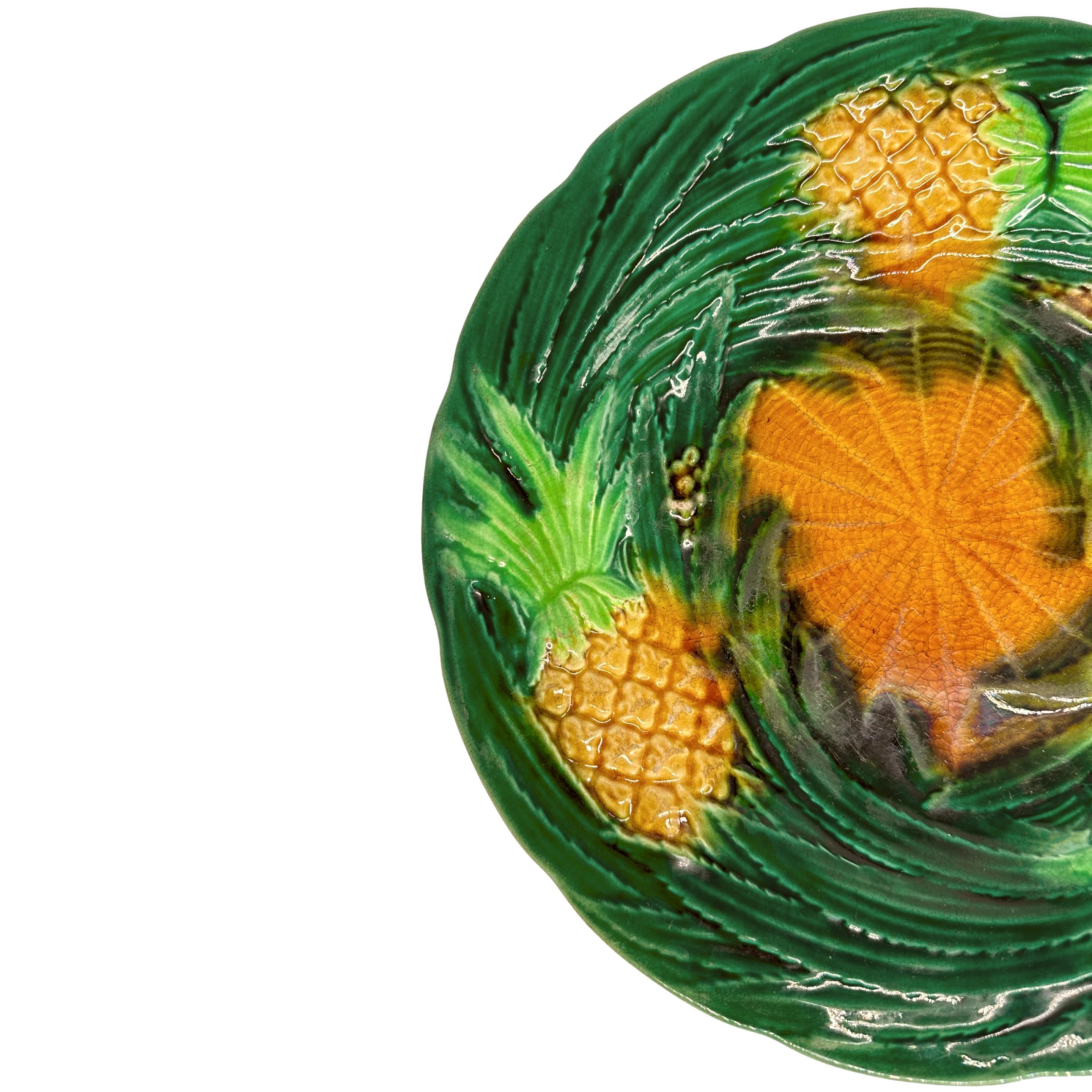 Assiette à dessert en majolique de George Jones, avec des ananas moulés en relief et des feuilles tourbillonnantes à glaçure verte, le centre avec une simulation de vannerie à glaçure ocre jaune, le revers portant le premier monogramme de GJ