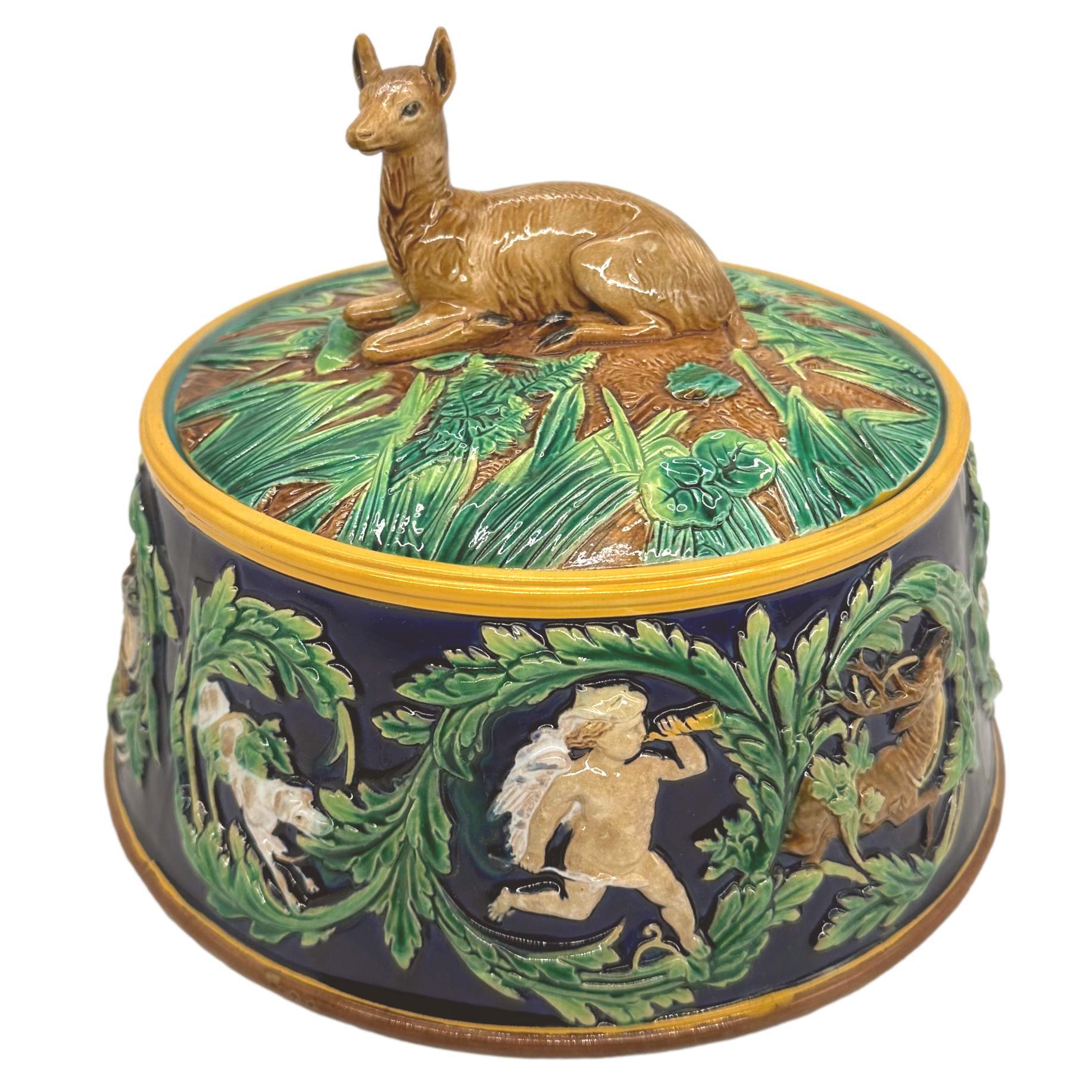 A George Jones Majolica Game Pie Tureen, the cover formed as a domed rustic mound with green glazed ferns and grasses, surmounted by a naturalistically molded and glazed recumbent doe, the base encircled with relief-molded images of Artemis, Greek