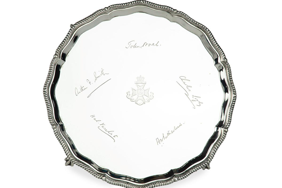 Silberne Präsentationsschale des King's Royal Rifle Corps (60th Regiment of Foot) in runder Form mit einem gadronierten Rand, auf vier Klauen- und Kugelfüßen stehend, in der Mitte ein Regimentsabzeichen mit einer Schlacht des Peninsula War und fünf