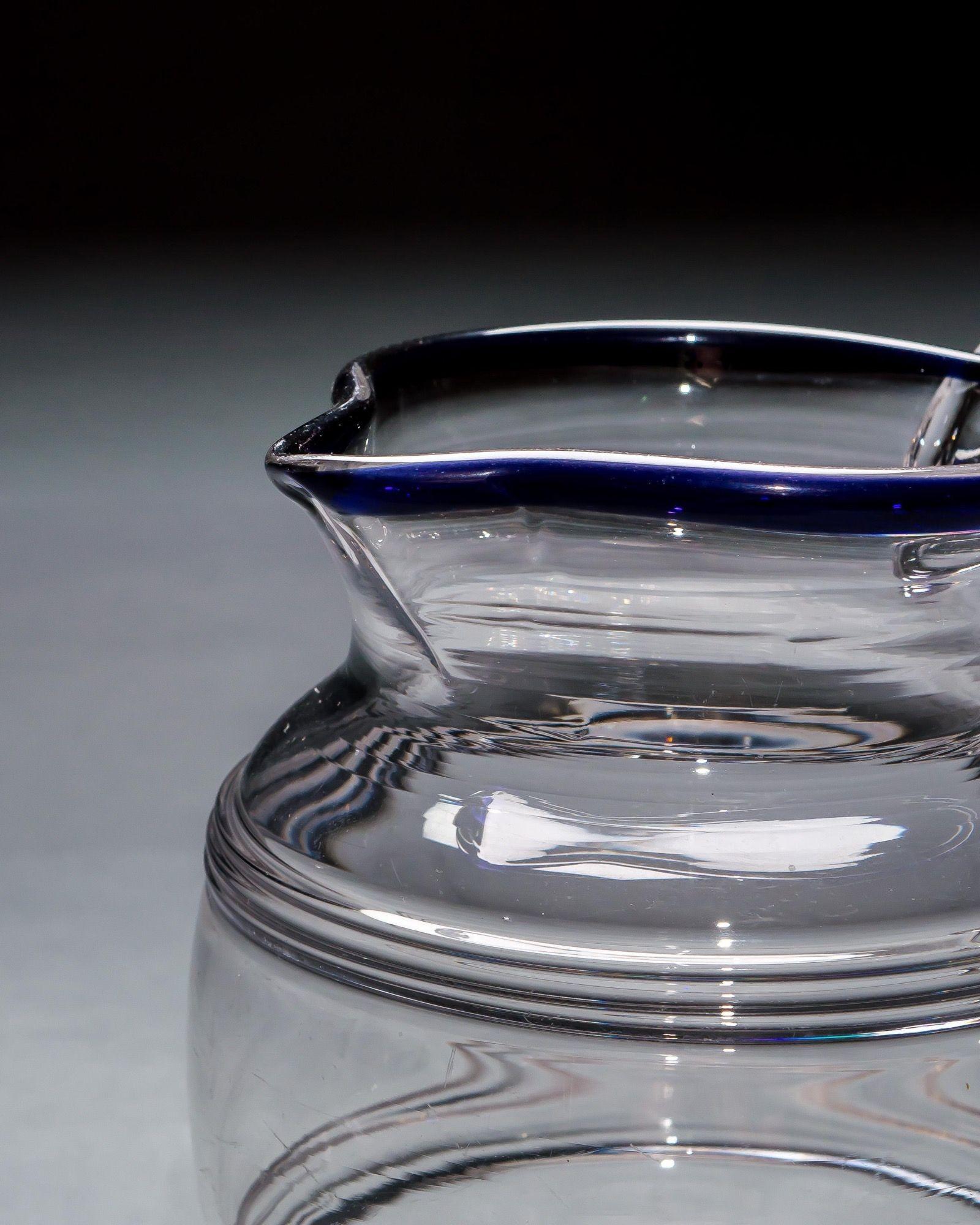 Una jarra de agua de cristal con el borde azul y dos anillos fresados.