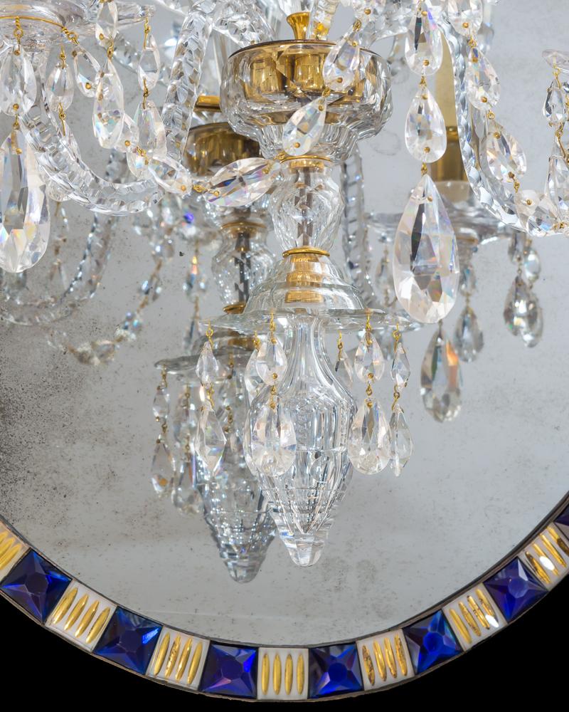 Un miroir ovale irlandais de l'époque géorgienne avec des segments blancs taillés superposés avec de la dorure appliquée alternant avec des bijoux bleus à facettes multiples, le miroir étant suspendu par un crochet doré à un lustre à deux lumières