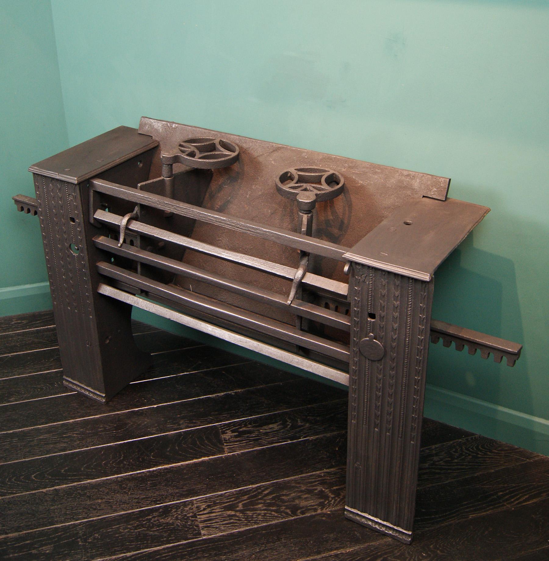 A well-preserved cast-iron Georgian kitchen fireplace range. The range with decorative cast-iron front panels and wrought-iron fire bars has adjustable side panels to alter the size of burning area, with hinged top fire-bar and circular kettle/pan