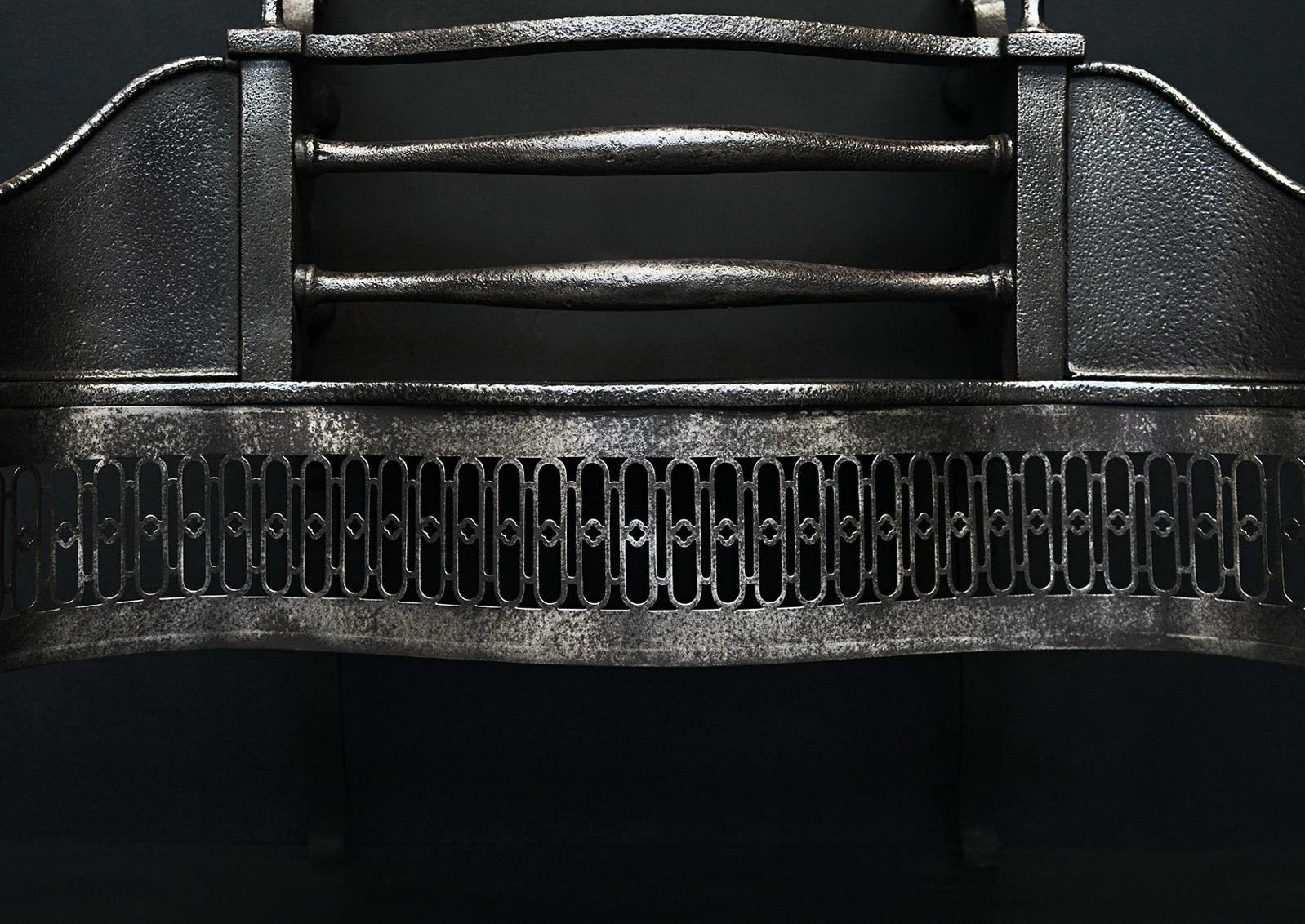A Georgian polished cast iron firegrate. The pierced, serpentine fret surmounted by bowed front bars and flanked by decorative side wings. The tapering legs with classical urn finials above. Plain back behind. Good quality, with a nice patina to