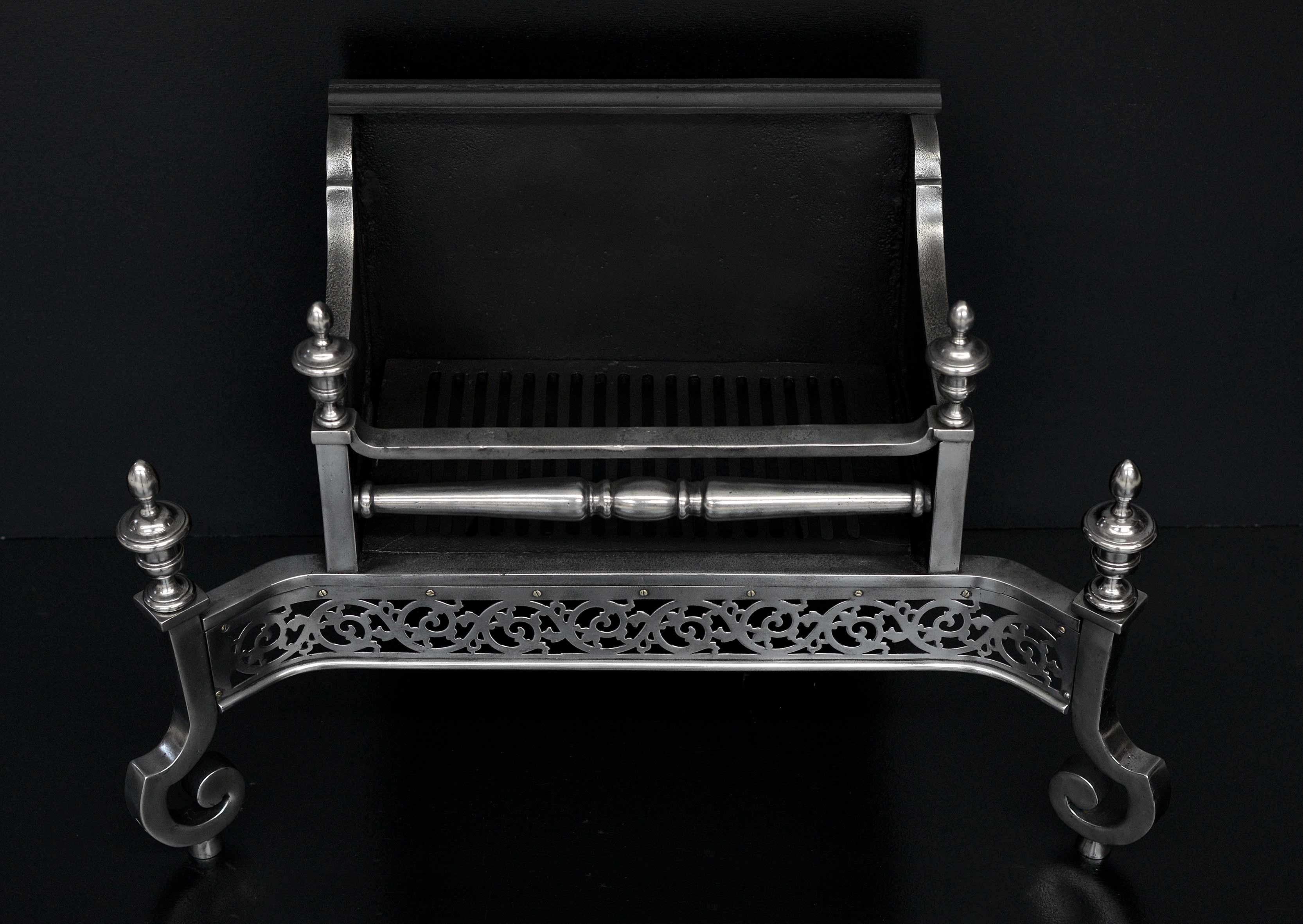 An English steel firegrate of Georgian form. The shaped legs surmounted by urn finials, the pierced fret with scrolled foliage throughout, with decorative cast front bar above. Cast iron fireback behind. Substantial burning area for a basket of