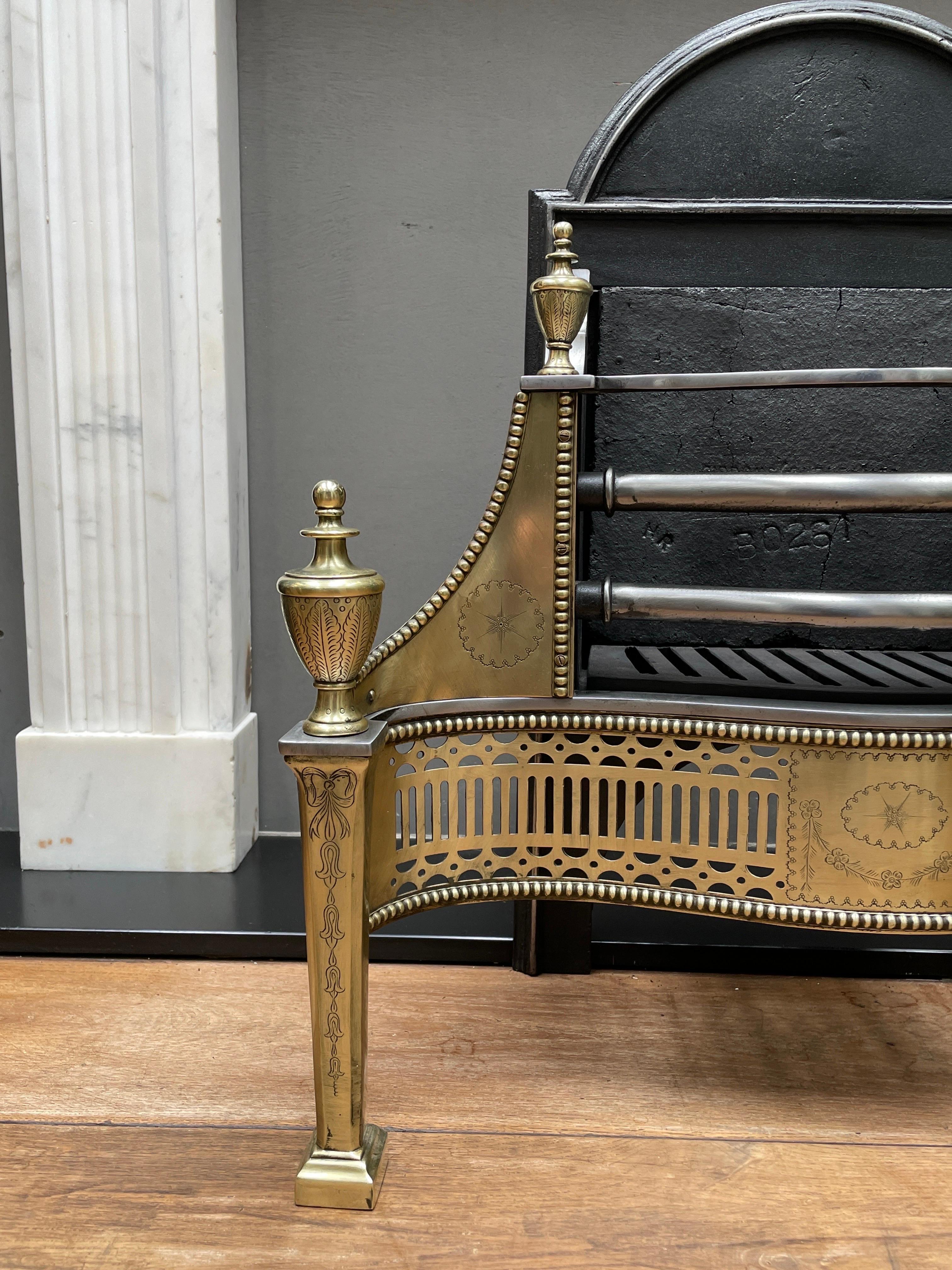 An engraved brass and steel Georgian style fire grate from the Mid-20th Century by blacksmiths Jordan and sons. The engraved front legs flanking a serpentine intricately pierced and cut fret with beaded edge. The conforming wings engraved and beaded