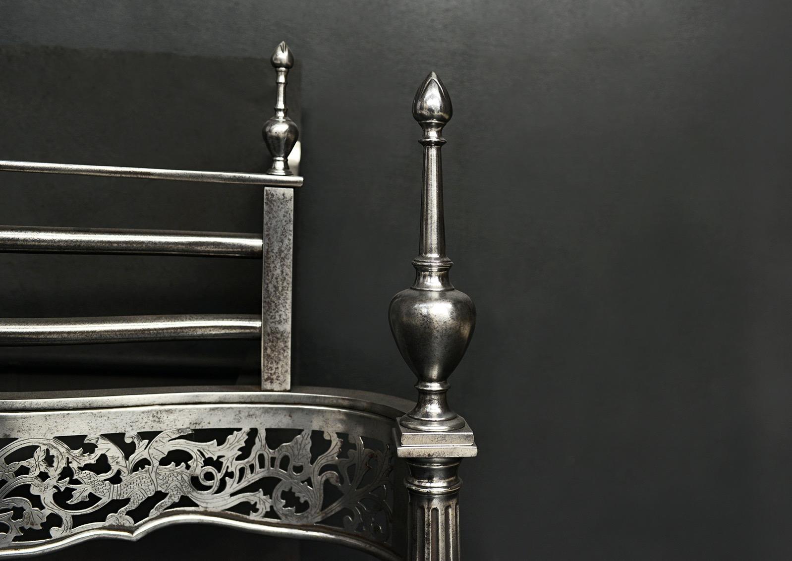A Georgian style polished steel firegrate. The pierced, shaped fret featuring mythical beasts and foliage. Tapered, fluted legs surmounted by tall finials. English. Modern.

Width At Front:	840 mm      	33 ⅛