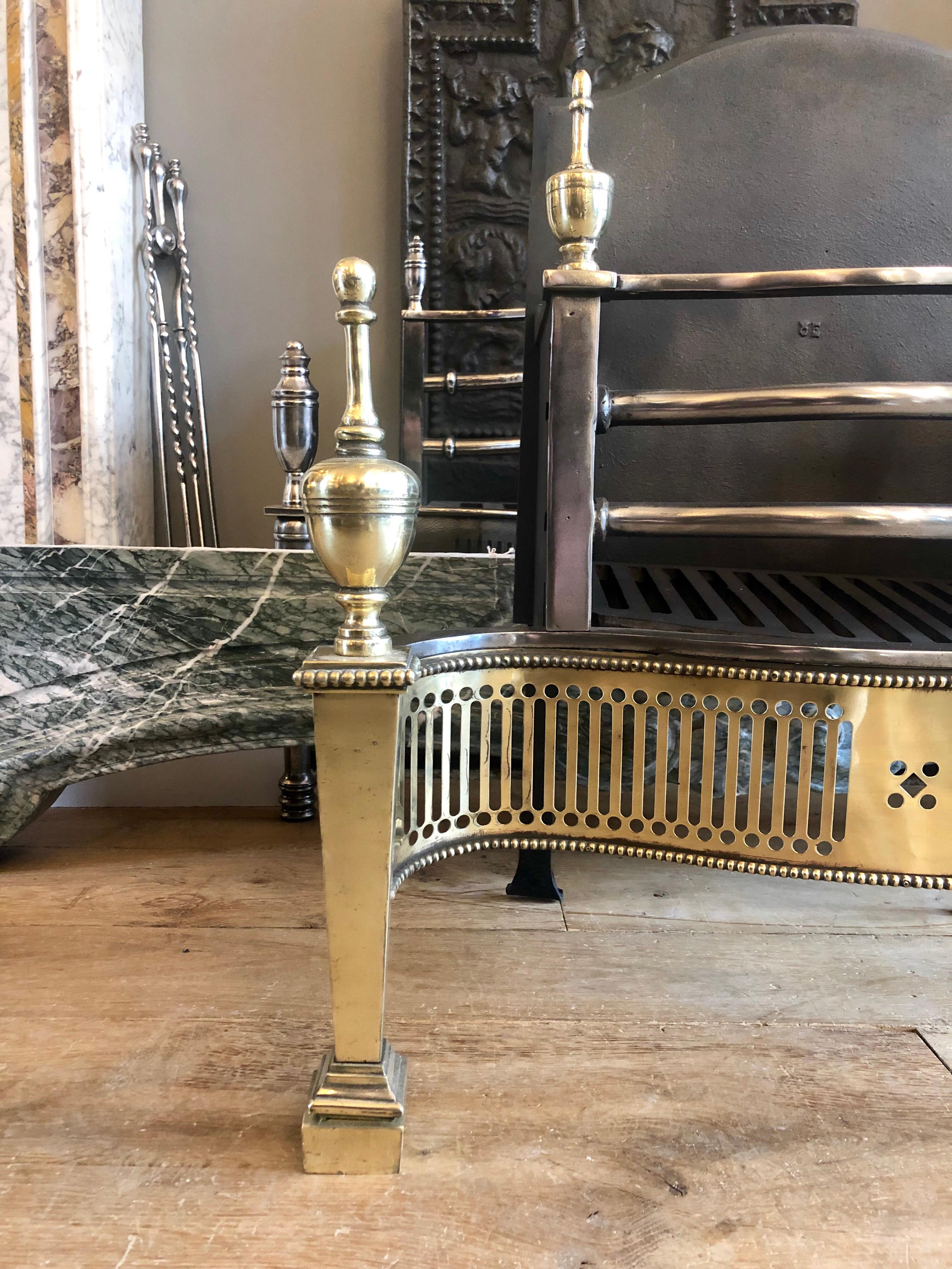 A good quality 20th century Georgian style fire grate with shaped and edged cast iron back, bow fronted steel bars, large brass urn finials and a pierced geometrical brass serpentine fret work.