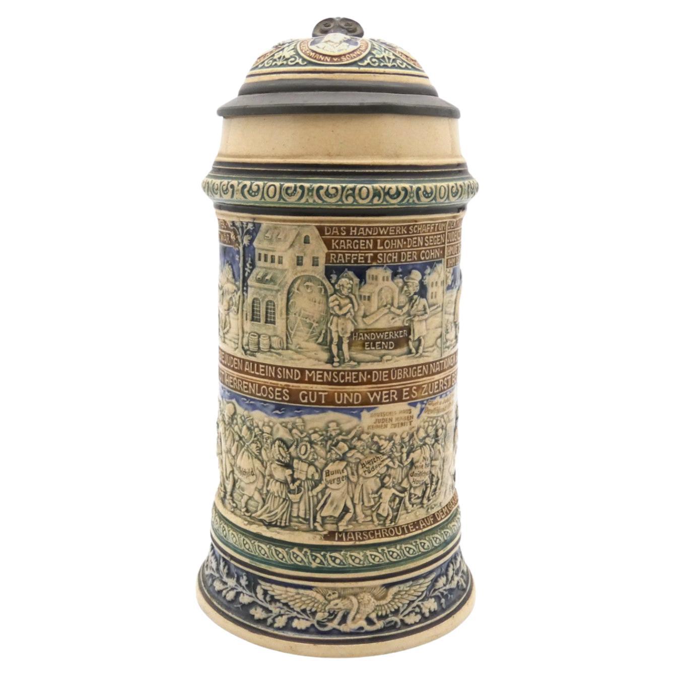 Late 19th-century ceramic beer stein with designs celebrating well-known antisemitic politicians, amid scenes of caricatured Jews growing rich by abusing, cheating, and stealing from Germans on the stein's upper half. 
On the lower half, the stein