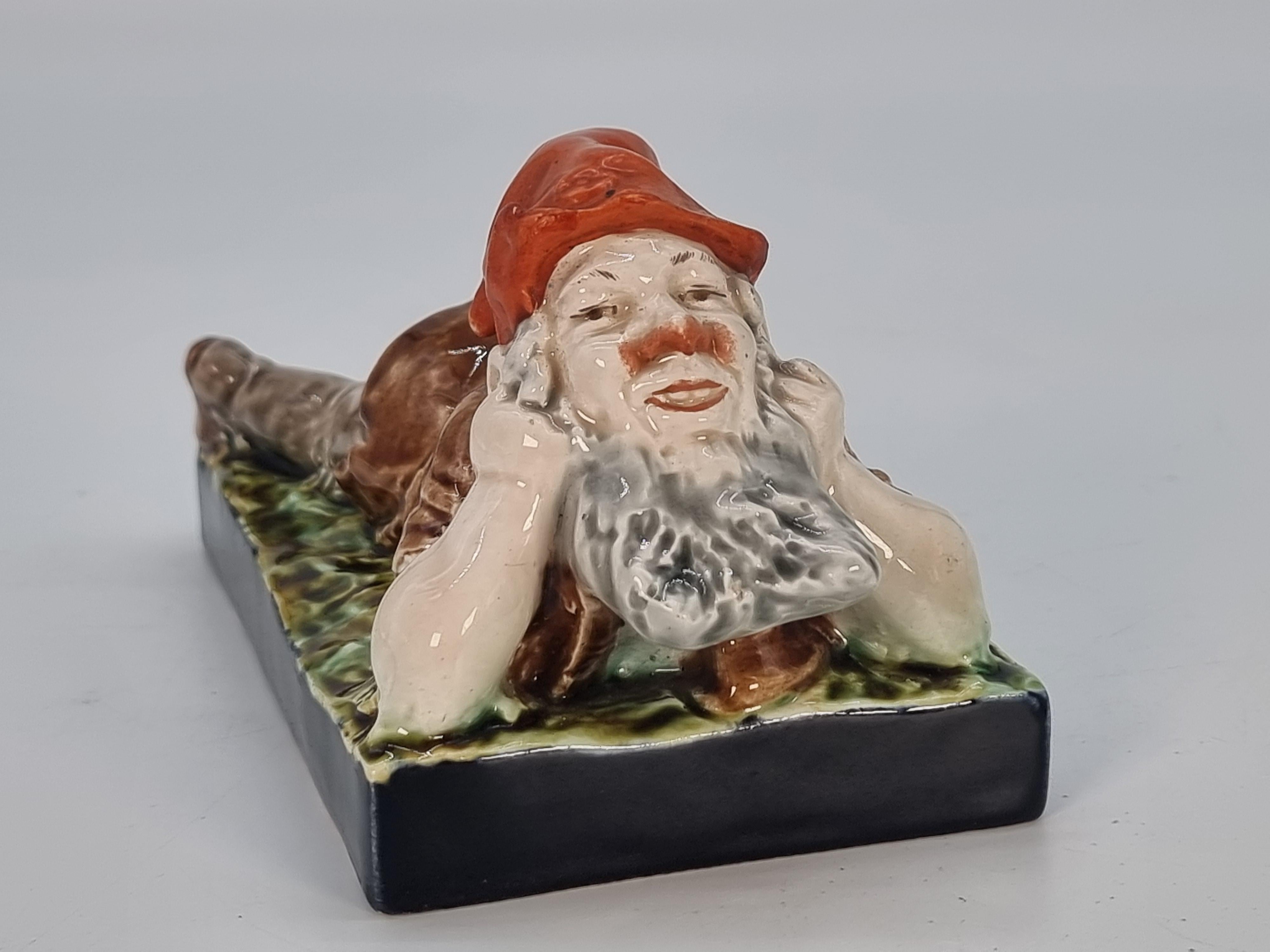 
This most unusual and very pleasing majolica pottery figure was made in Germany or Austria circa 1880 and it depicts a happy rosy cheeked gnome lying down on his front with his head raised supported by his hands from bent elbows. He has a happy