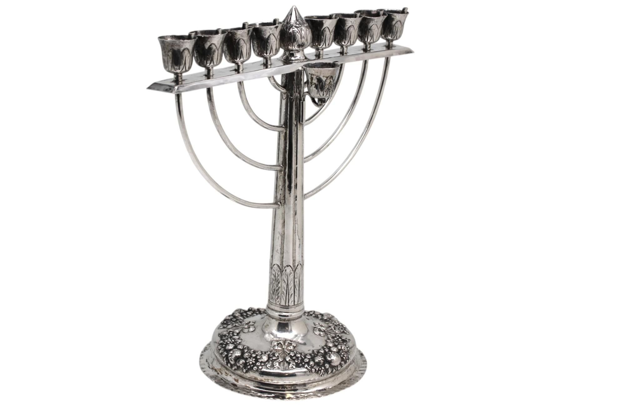 This elegant German silver Hanukkah lamp, crafted around 1900, is a masterful blend of classical refinement and symbolic reverence, drawing deeply from both natural motifs and the sacred traditions of the Temple menorah.

The lamp is set on a