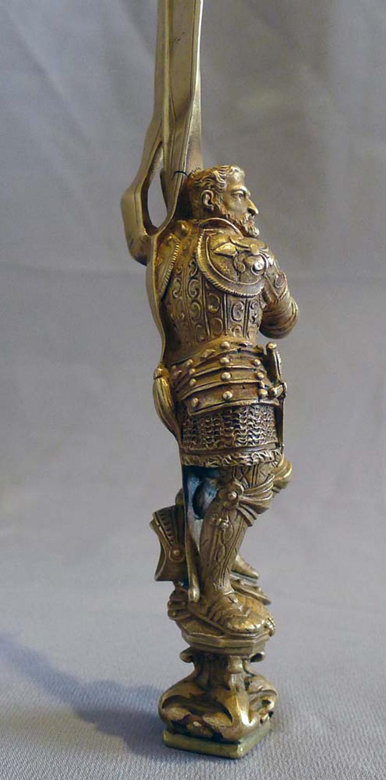 Un très beau et inhabituel coupe-papier et sceau en bronze doré représentant un chevalier médiéval en armure tenant une bannière. Le chevalier est debout sur une base à volutes, un pied sur un bouclier et un casque à plumes derrière. Il tient la