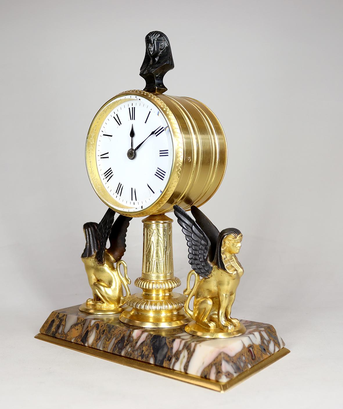 Eine ägyptische Revival-Uhr in einem vergoldeten und bronzenen Gehäuse. Das viersäulige Acht-Tage-Werk mit Zylinderhemmung ist in einem Trommelgehäuse untergebracht und hinter einem strahlend weißen Emailzifferblatt mit römischen Ziffern und