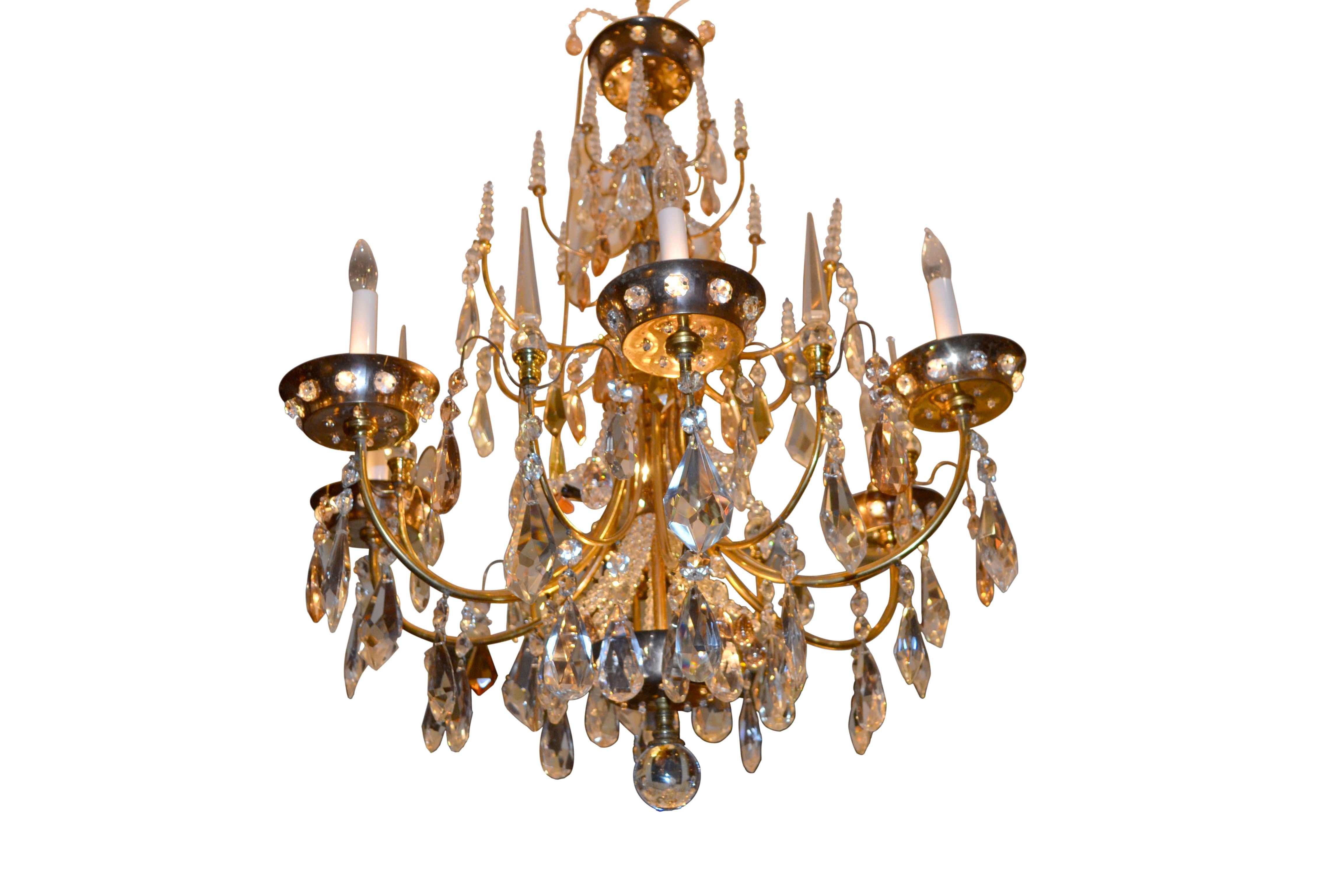 A gilded metal and crystal chandelier of classical design typical of fixtures from the 1920s made by the company Baguès in Paris, the leading lighting firm during the first half of the 20th century. The central stem supports four tiers of decorative
