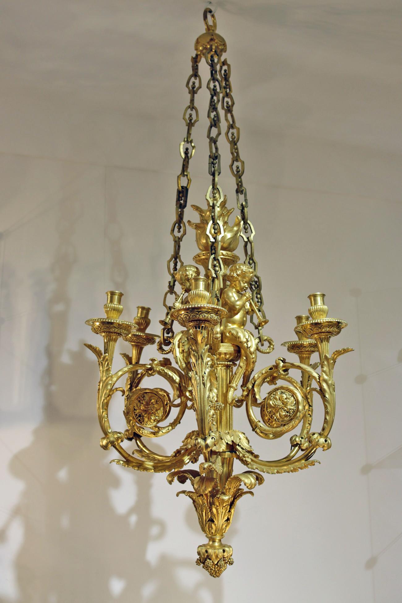 A gilt bronze chandelier with six winding lights surmounted by child blowers seated on a cylindrical fluted shaft finished with a base decorated with foliage and bunches of grapes; (small missing chains; pierced for the electricity).

Louis XV