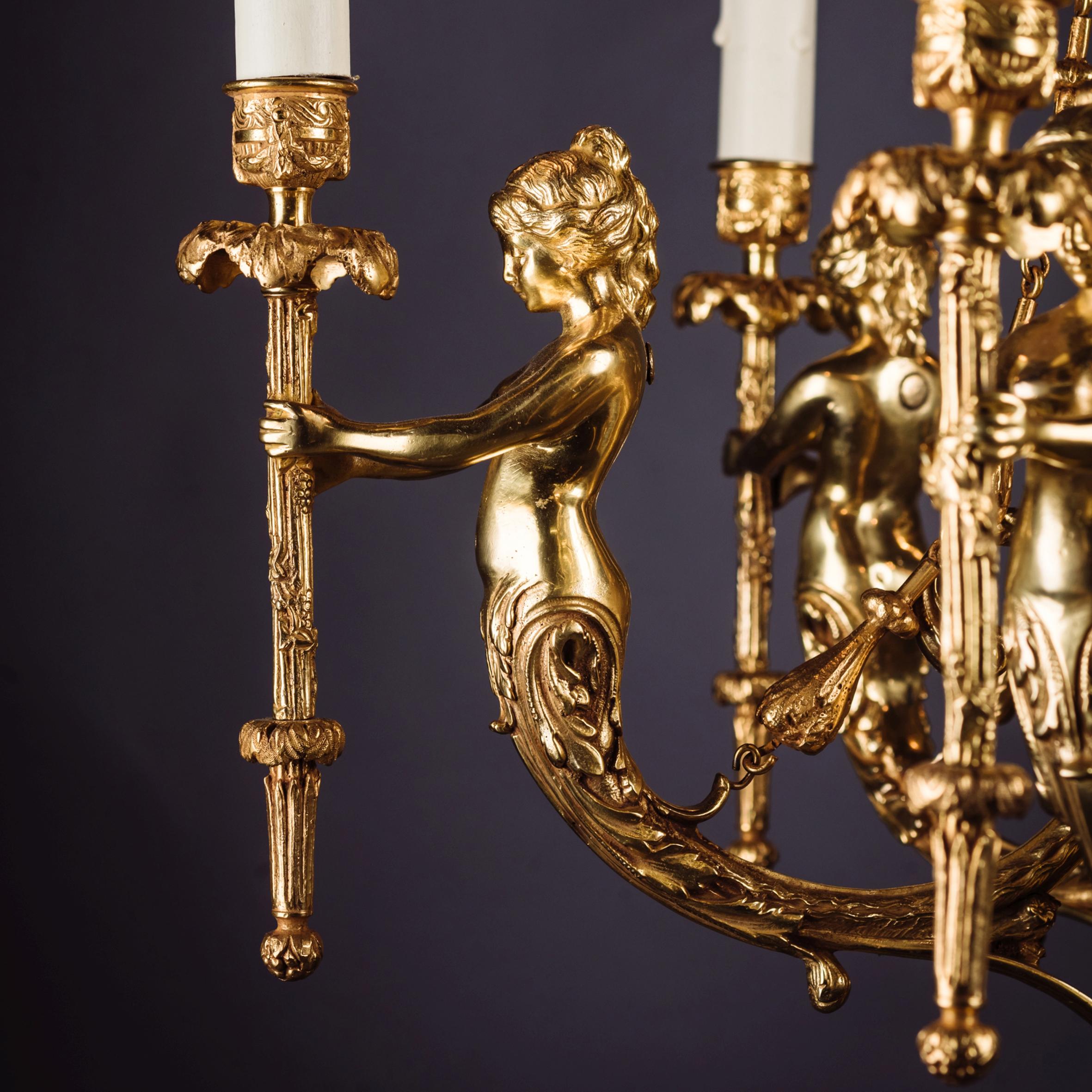 A fine gilt-bronze figural six-light figural chandelier.

The chandelier has an acanthus cast finial above a domed corona, finely cast with drapery and suspending bellflower chains, above a central stem and ovoid urn. The urn issuing six scrolling