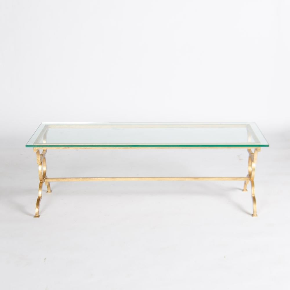 A beautiful gilt iron open rectangular glass top coffee table, framed with ring motif legs and a single stretcher after Gilbert Poillerat, France.