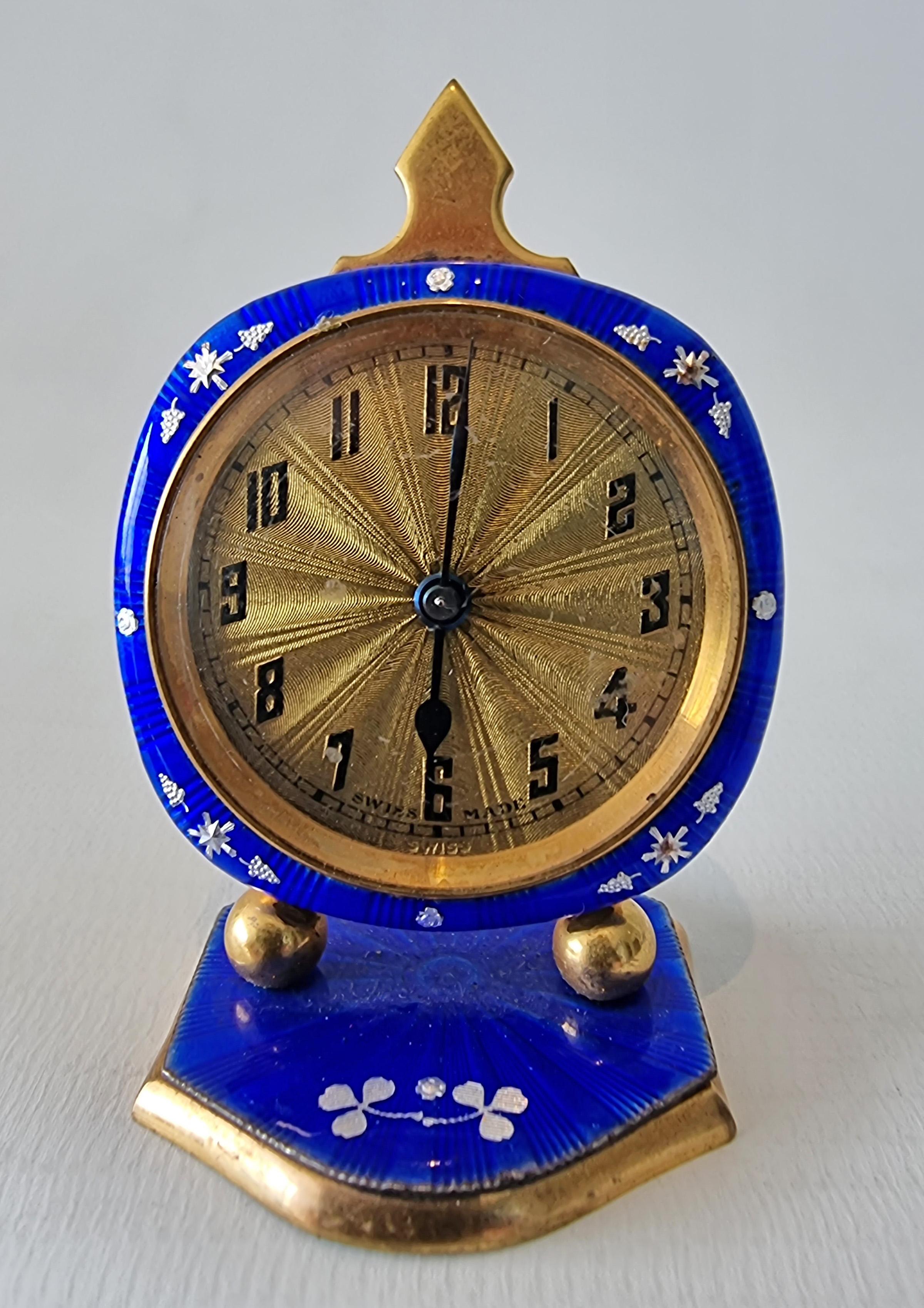 A small blue guilloche enamel gilt metel sub miniature boudoir clock. With overpainted silver flowers on the engine turned enamel, the gilt dial engine turned with starburst effect and arabic numerals, marked swiss made below 6 o clock. 30 hour