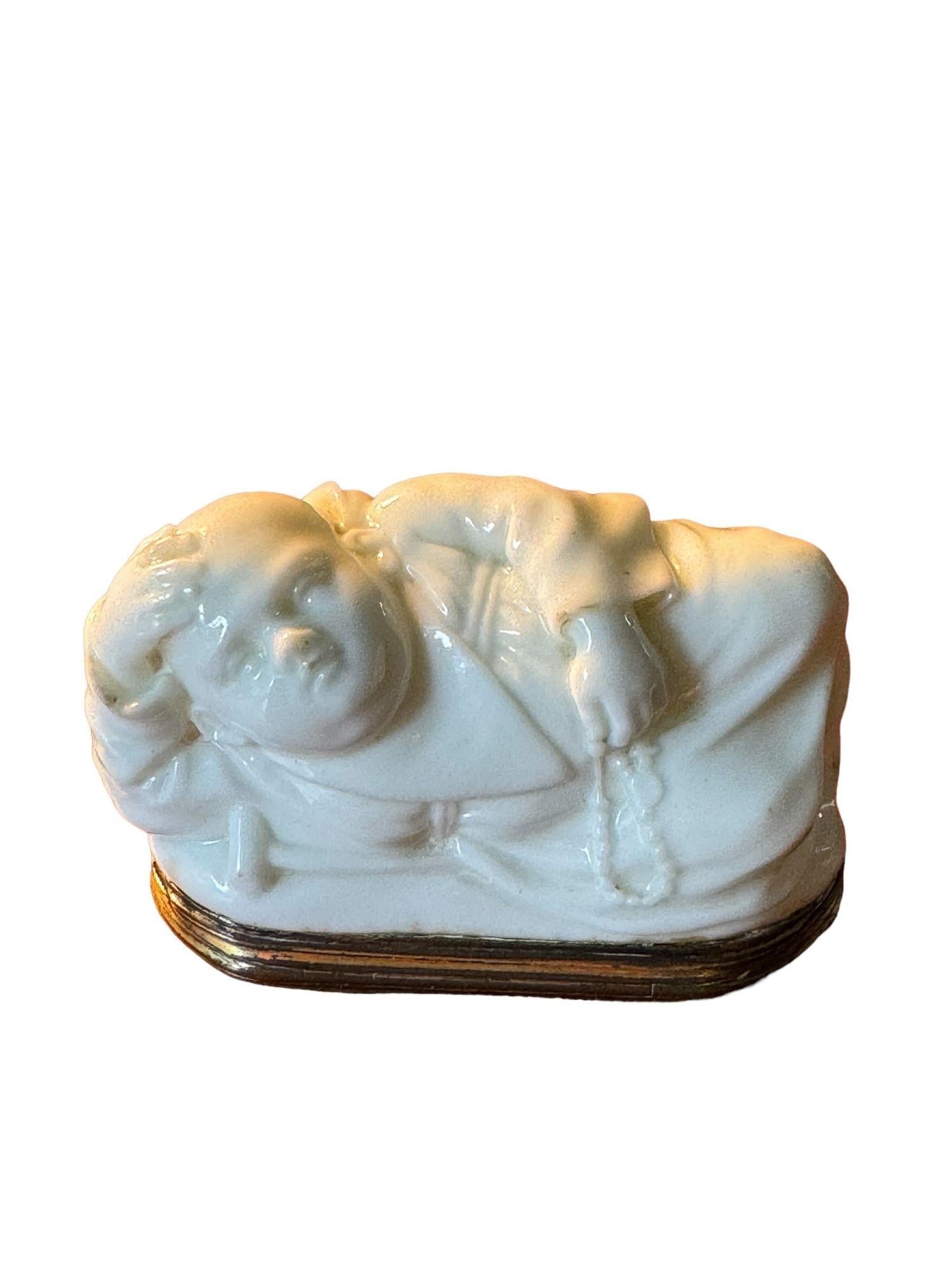 A GILT-METAL MOUNTED SNUFF BOX
Circa 1750, probably Saint-Cloud
Modelled as a reclining monk, one hand supporting his bald head, the other holding a rosary and with a crutch at his side, the interior lid painted in puce camaïeu with a harbor scene