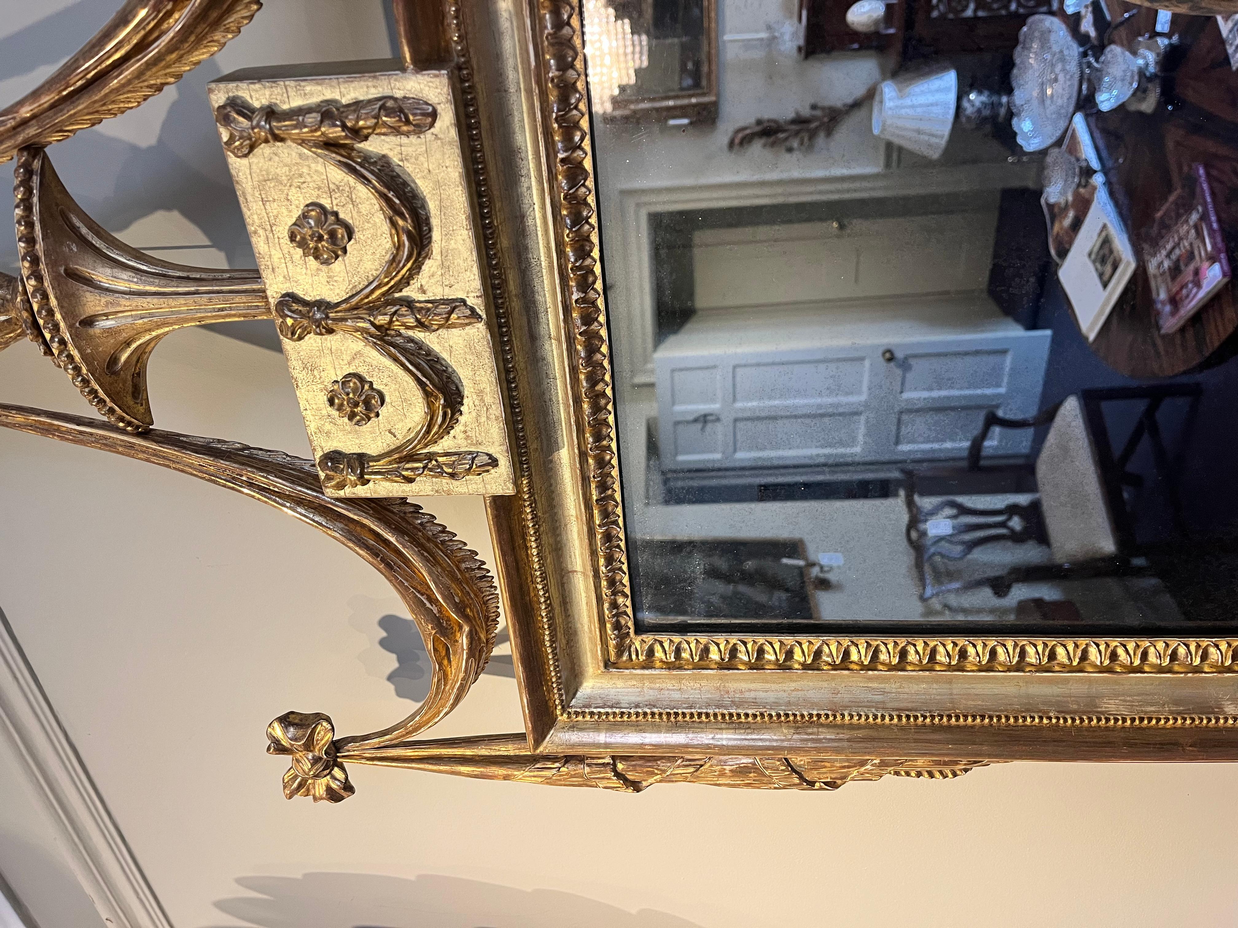 An extremely decorative carved and giltwood overmantle mirror.

The mirror features a classical flamed urn with ribboned drapery decorations and  two tone gilding throughout.

