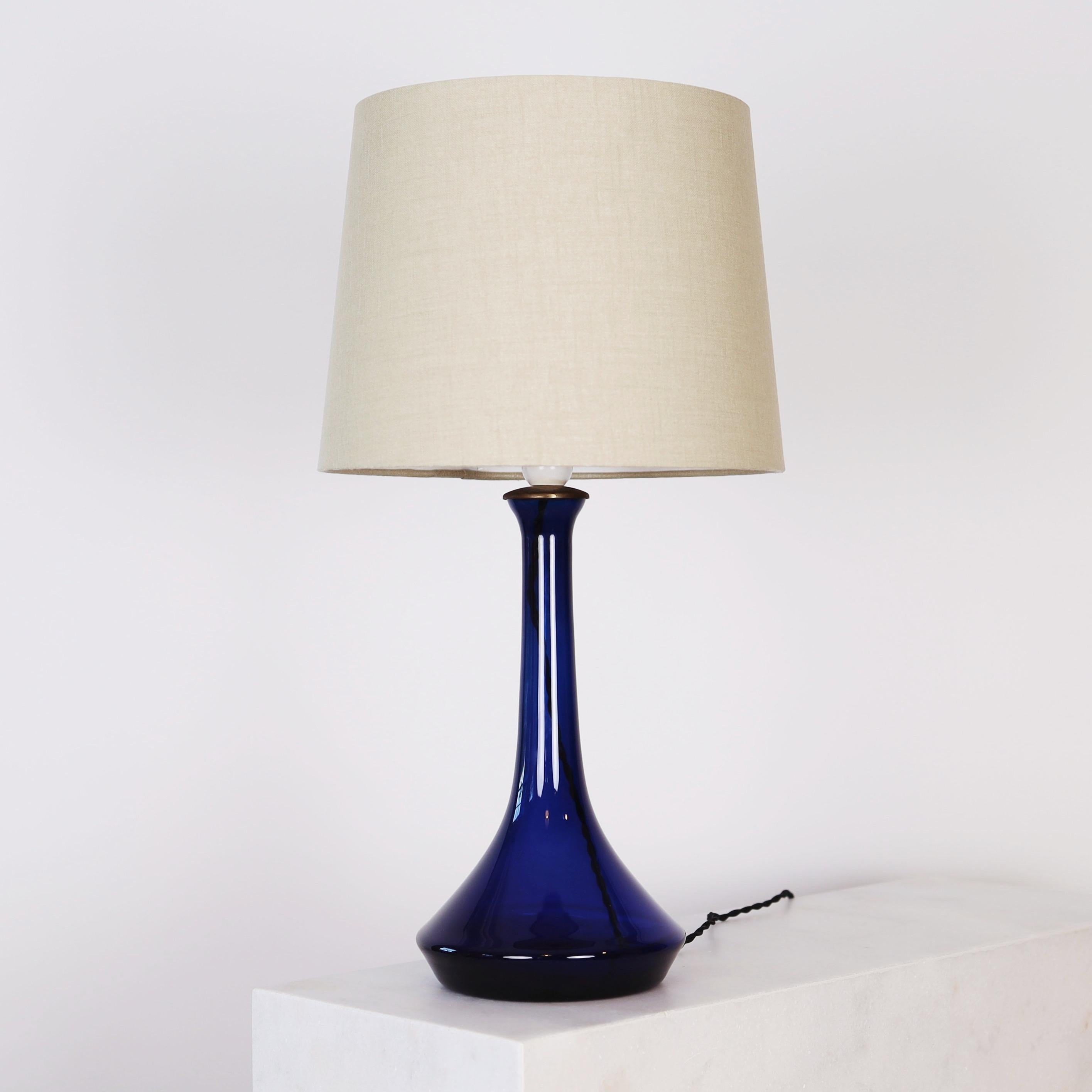 A dark blue glass desk lamp designed by Lisbeth Brams in 1966 for Fog & Mørup. The eye-catching piece is one of three in her trio for Fog & Mørup. We have the trio available. 

* A dark blue glass table lamp with a brass top and a beige fabric