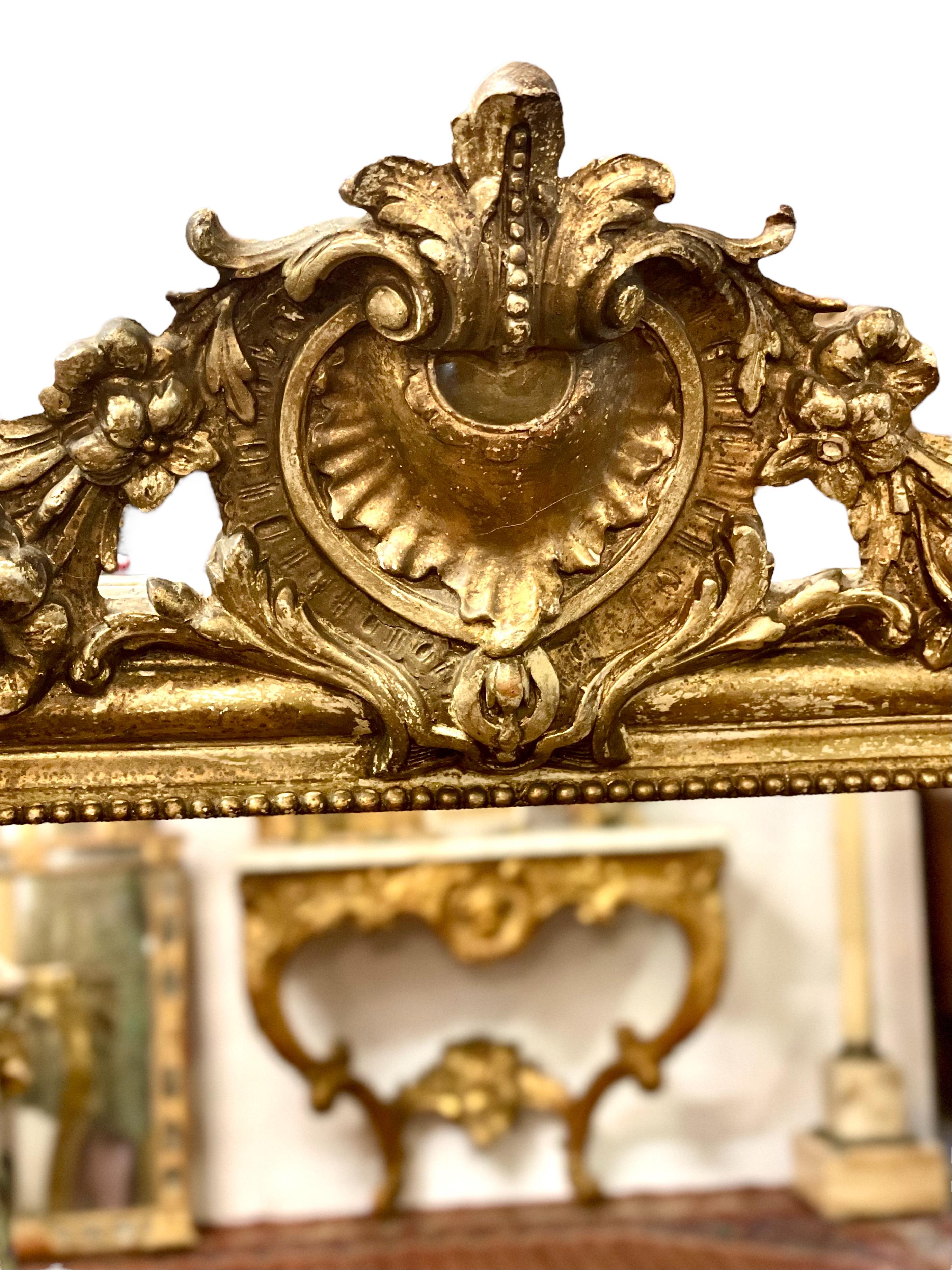 A gleaming 19th century Louis Philippe gilt mirror with extravagant shell and flower cartouche. Typical of the style, this beautiful mirror features the elegantly rounded upper corners and clean lines of the period, and features the classic